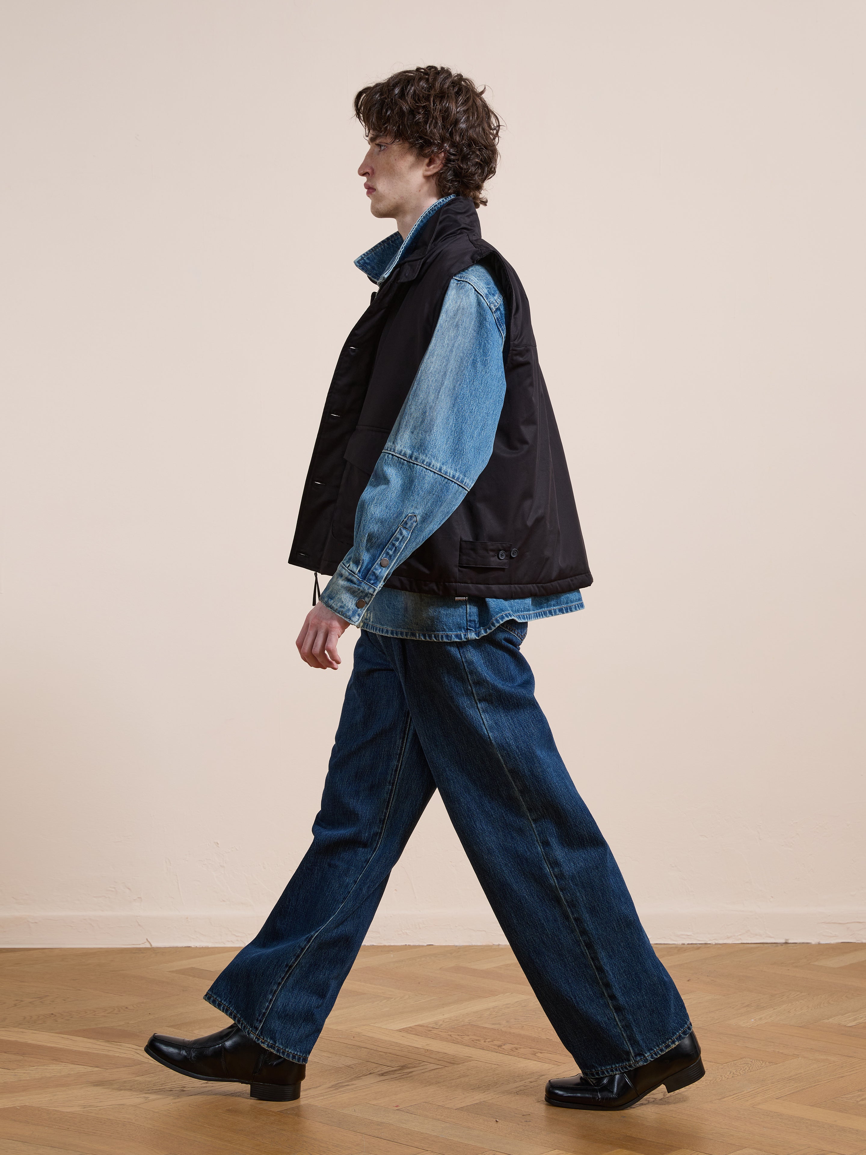 Wearing FOUND's Padded Cargo Vest over a denim shirt, wide-leg jeans, and black heeled boots, a person walks across a wooden floor against a plain light background.