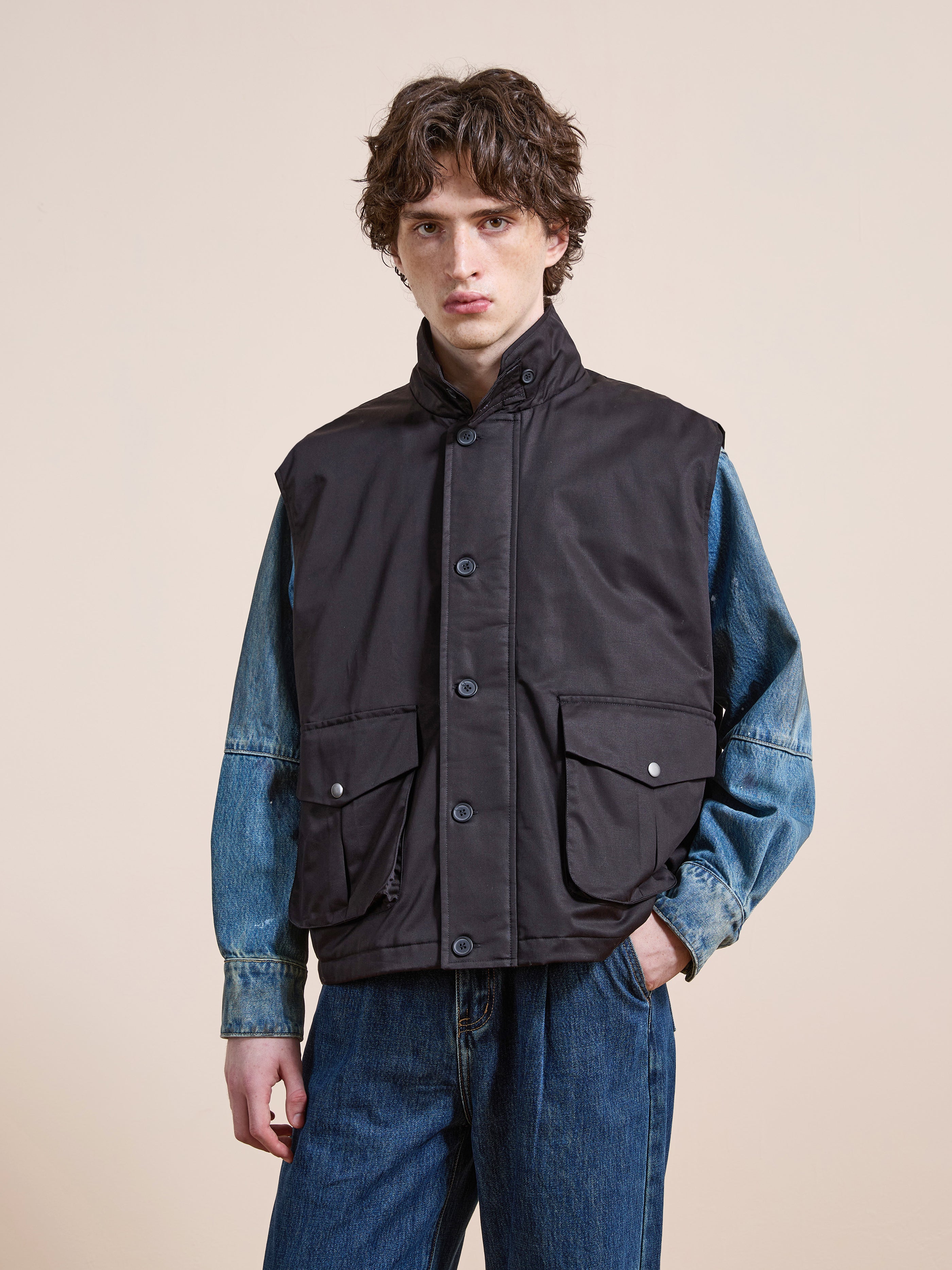 Someone wearing the FOUND Padded Cargo Vest in black over a blue denim jacket and blue jeans stands against a plain light background.