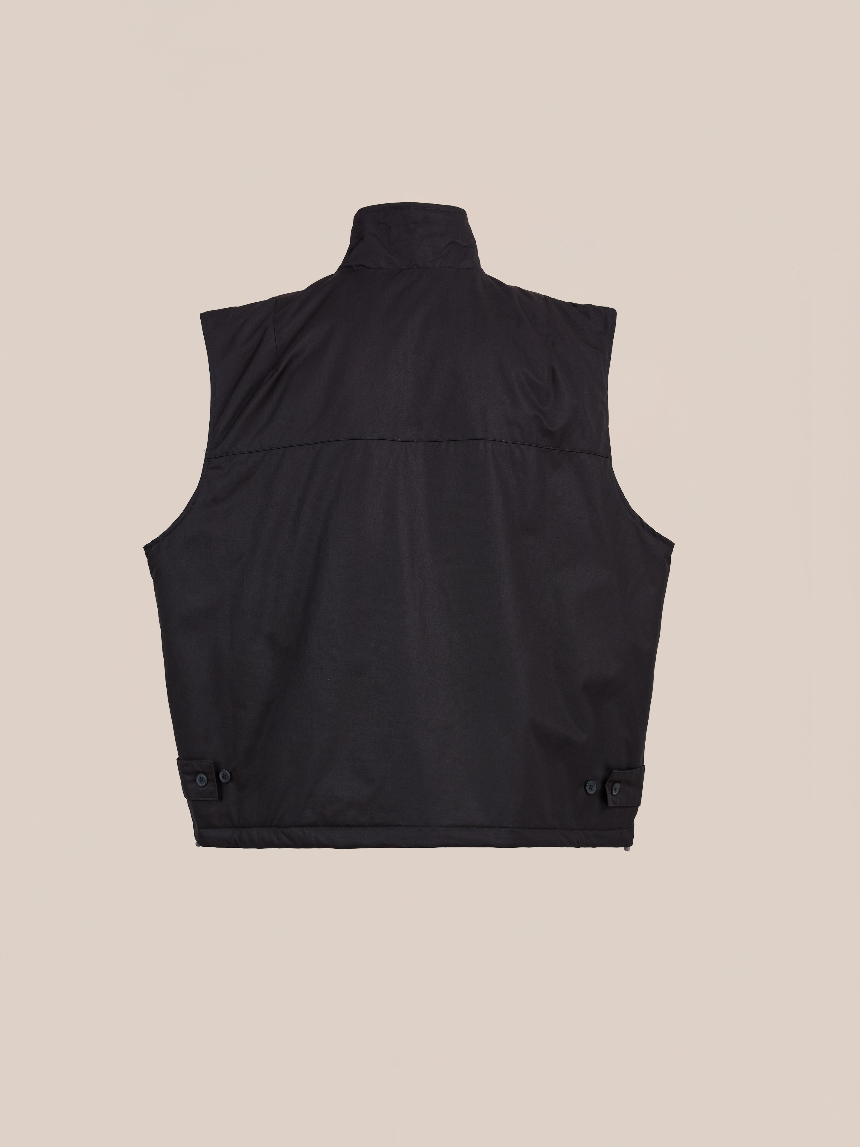 FOUND Padded Cargo Vest in black cotton twill shown from the back, with a high collar, straight hem, and adjustable button side tabs—ideal for layering. Displayed on a plain beige background.