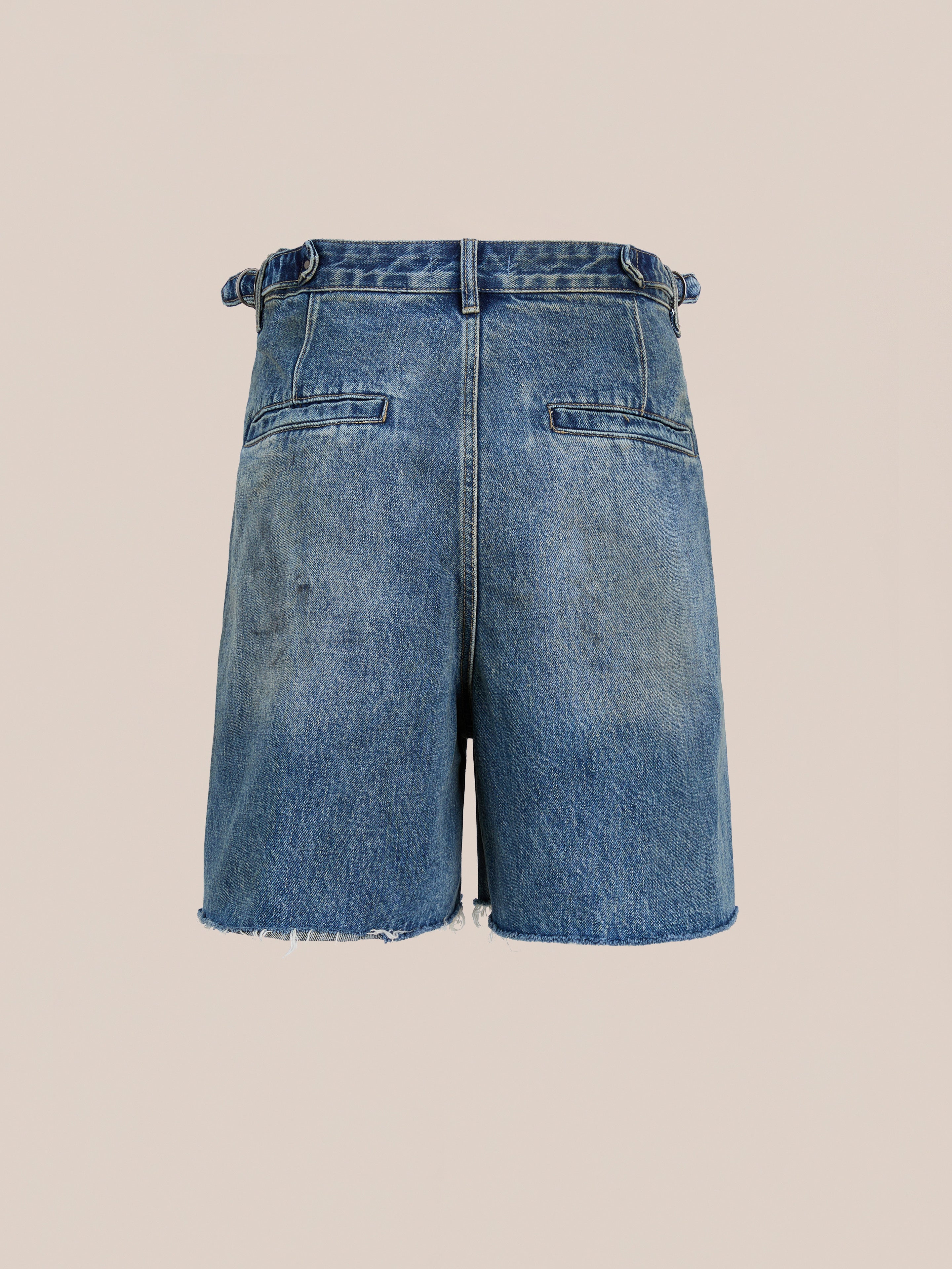 Back view of Found's Paint Studio Denim Shorts in vintage blue with frayed hems, two back welt pockets, and belt loops, shown against a plain beige background.