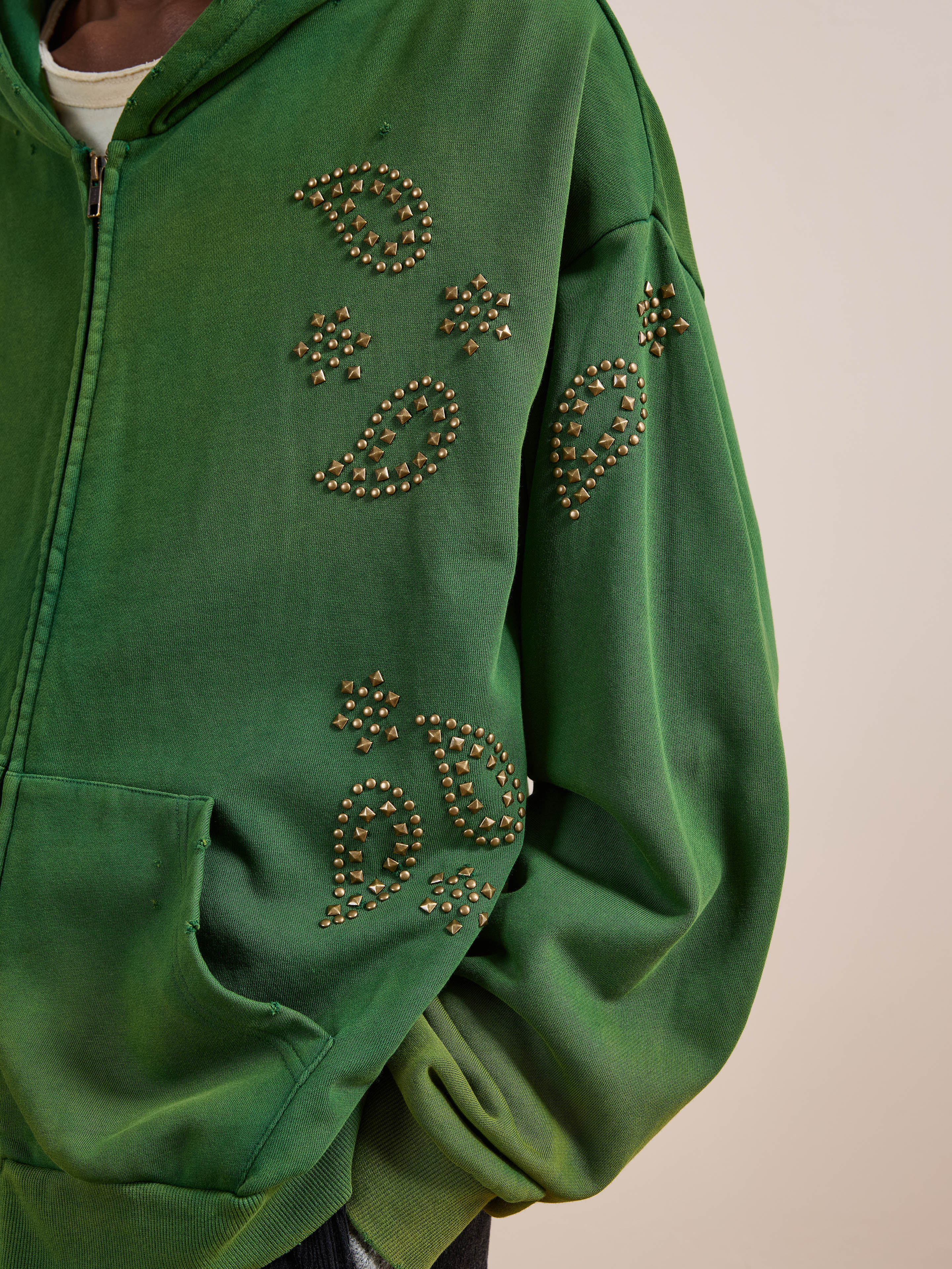 A person wears the FOUND Paisley Studded Zip Up Hoodie in green, a unisex relaxed fit hoodie combining vintage style with star accents and bold studded paisley details for a standout look.