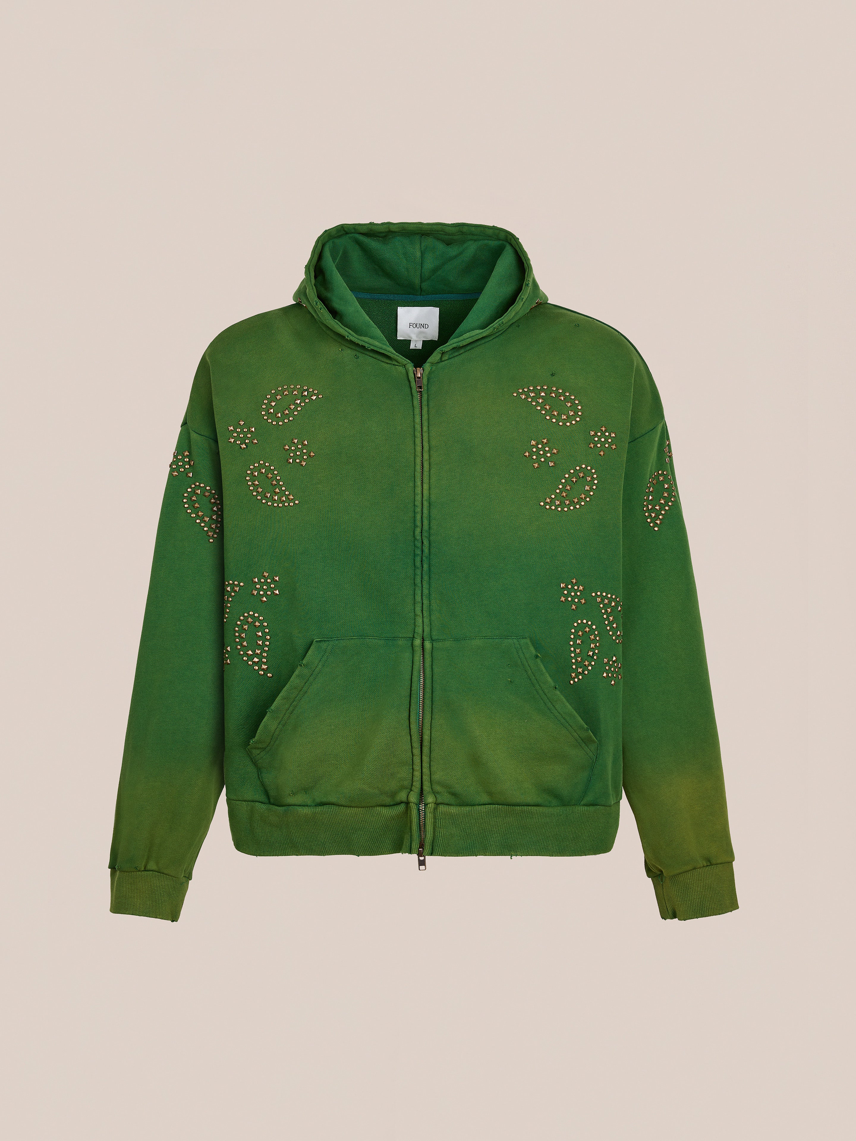 The FOUND Paisley Studded Zip Up Hoodie in green features front pockets and paisley-shaped metal studs on the chest, sleeves, and shoulders. This unisex relaxed fit hoodie is shown against a beige background for a vintage vibe.