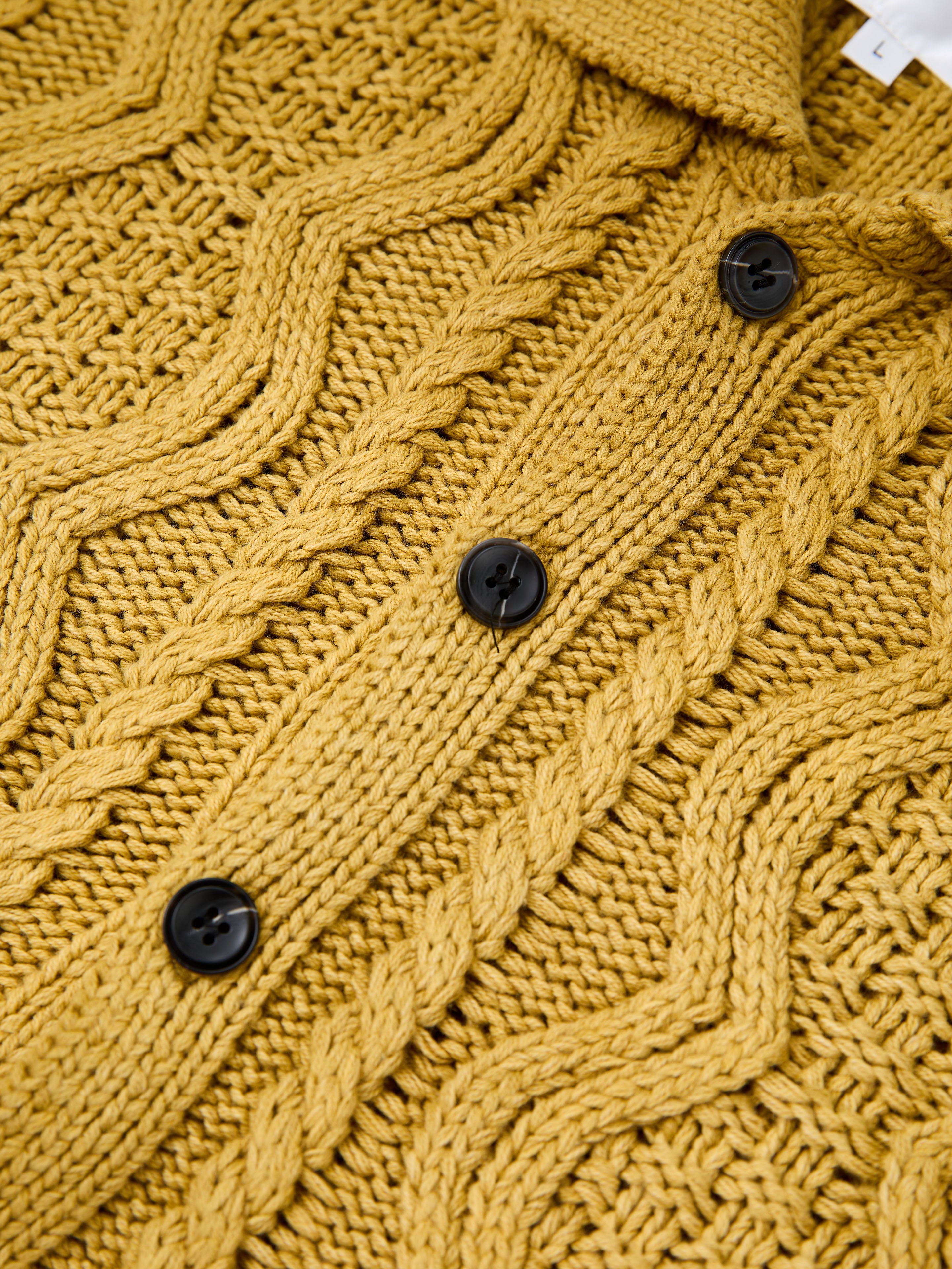 Close-up of the FOUND Cable Knit Buttoned Cardigan in yellow, showcasing chunky cable knitting, black buttons, and a textured design.
