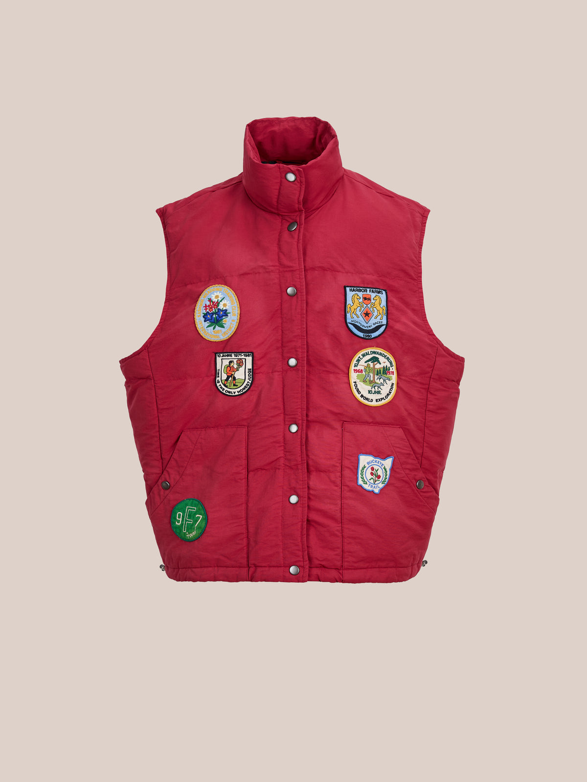 FOUND Patch Down Vest: Sleeveless red outdoor vest with six colorful embroidered patches on the front, shown on a plain beige background.