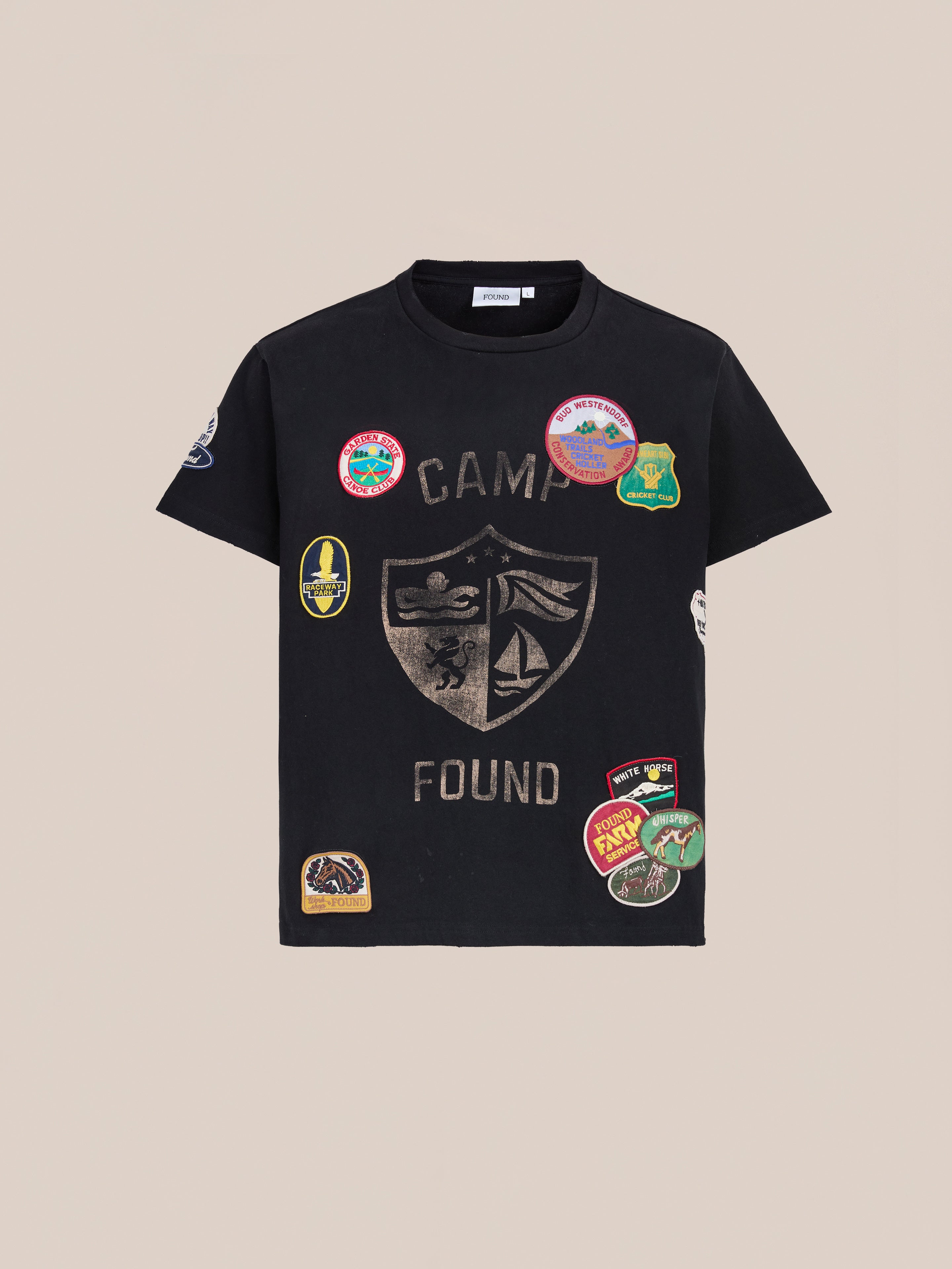 The Patchwork Camp Tee by FOUND is a vintage black unisex relaxed-fit shirt, showcasing a crest and “Camp Found” text with colorful embroidered patches on the front and sleeves.