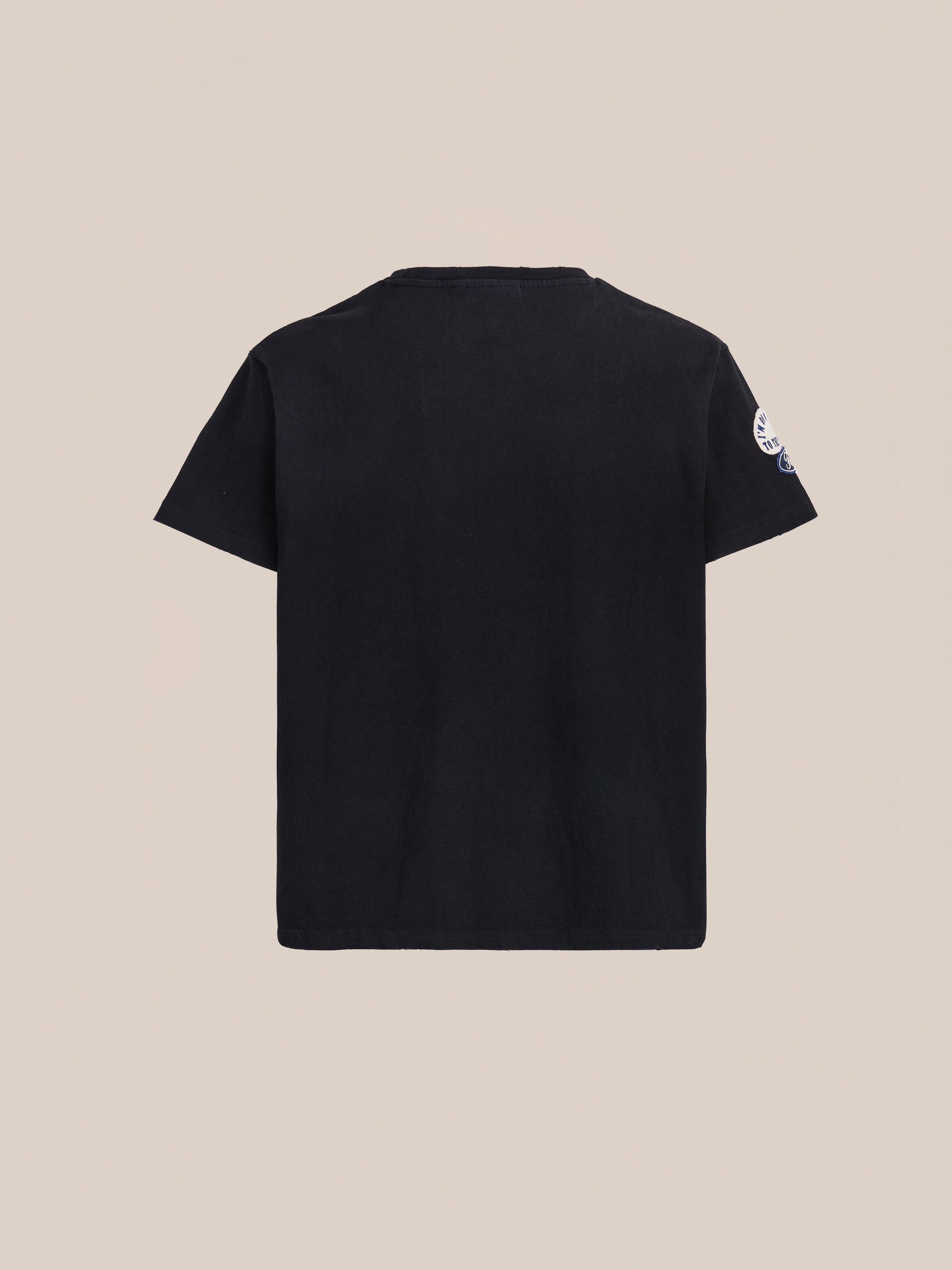 The FOUND Patchwork Camp Tee, a unisex relaxed fit in vintage black, is shown from the back against a light beige background.