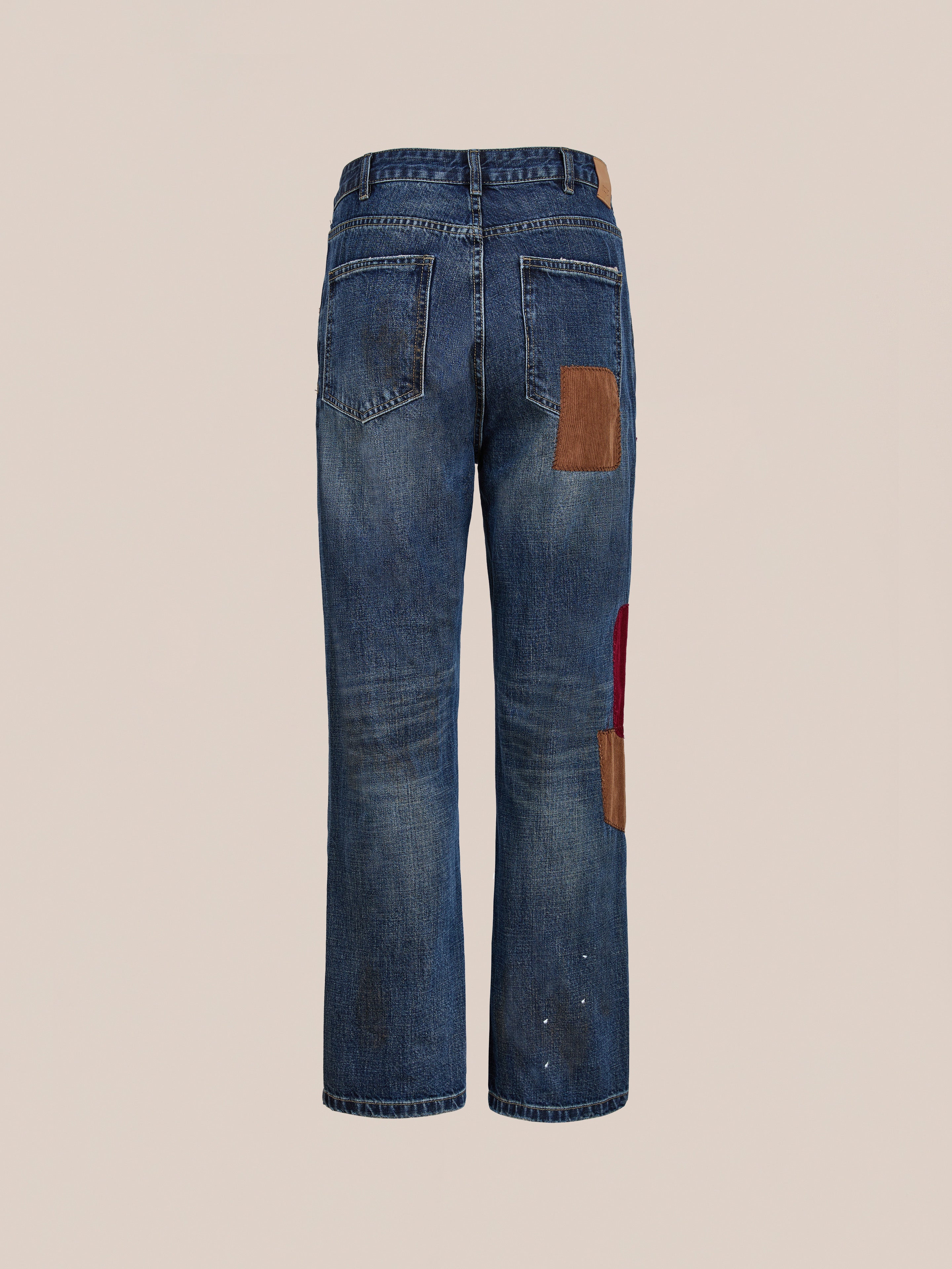 Back view of FOUND Patchwork Jeans, a unisex vintage denim style featuring brown and red patchwork details on the pockets and legs, displayed against a plain beige background.