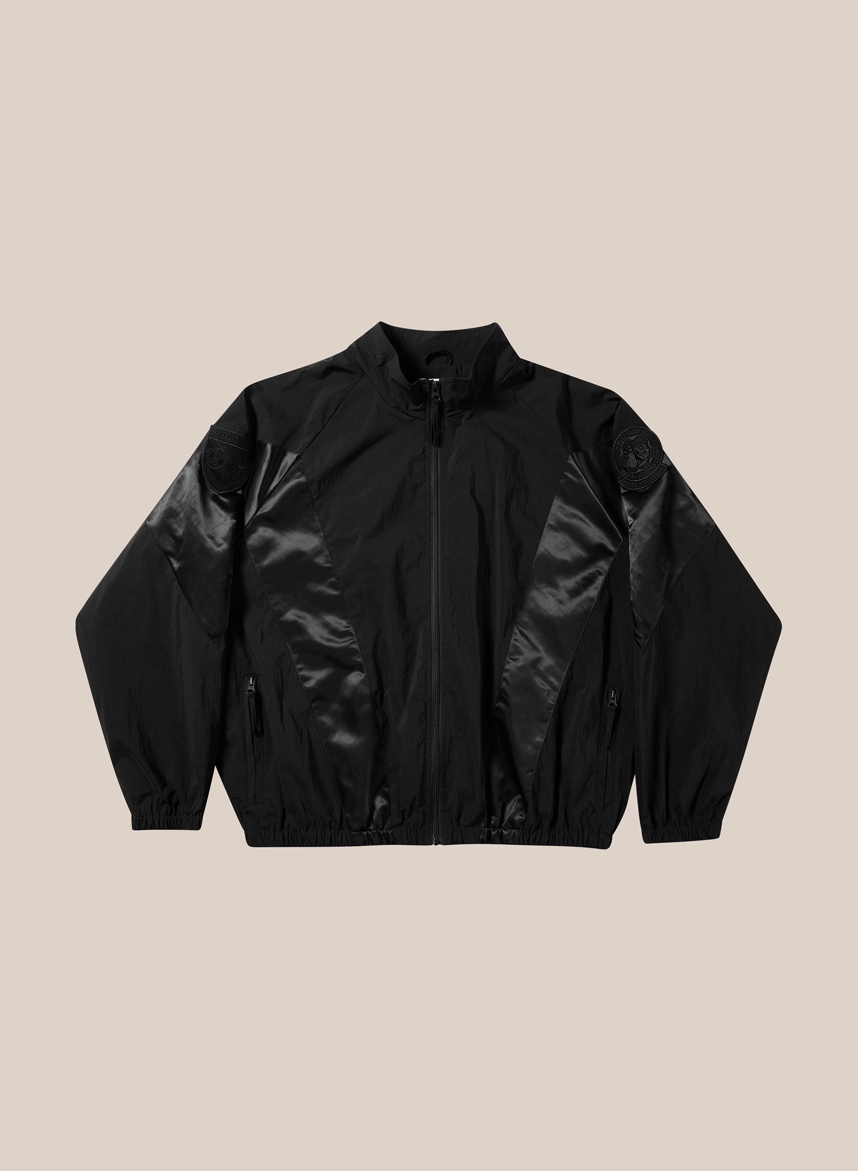 The FOUND Pine and Rose Jacket is a black unisex windbreaker featuring a high collar, elastic cuffs and hem, shiny front and sleeve panels, and zippered pockets—ideal for vintage sportswear style fans.