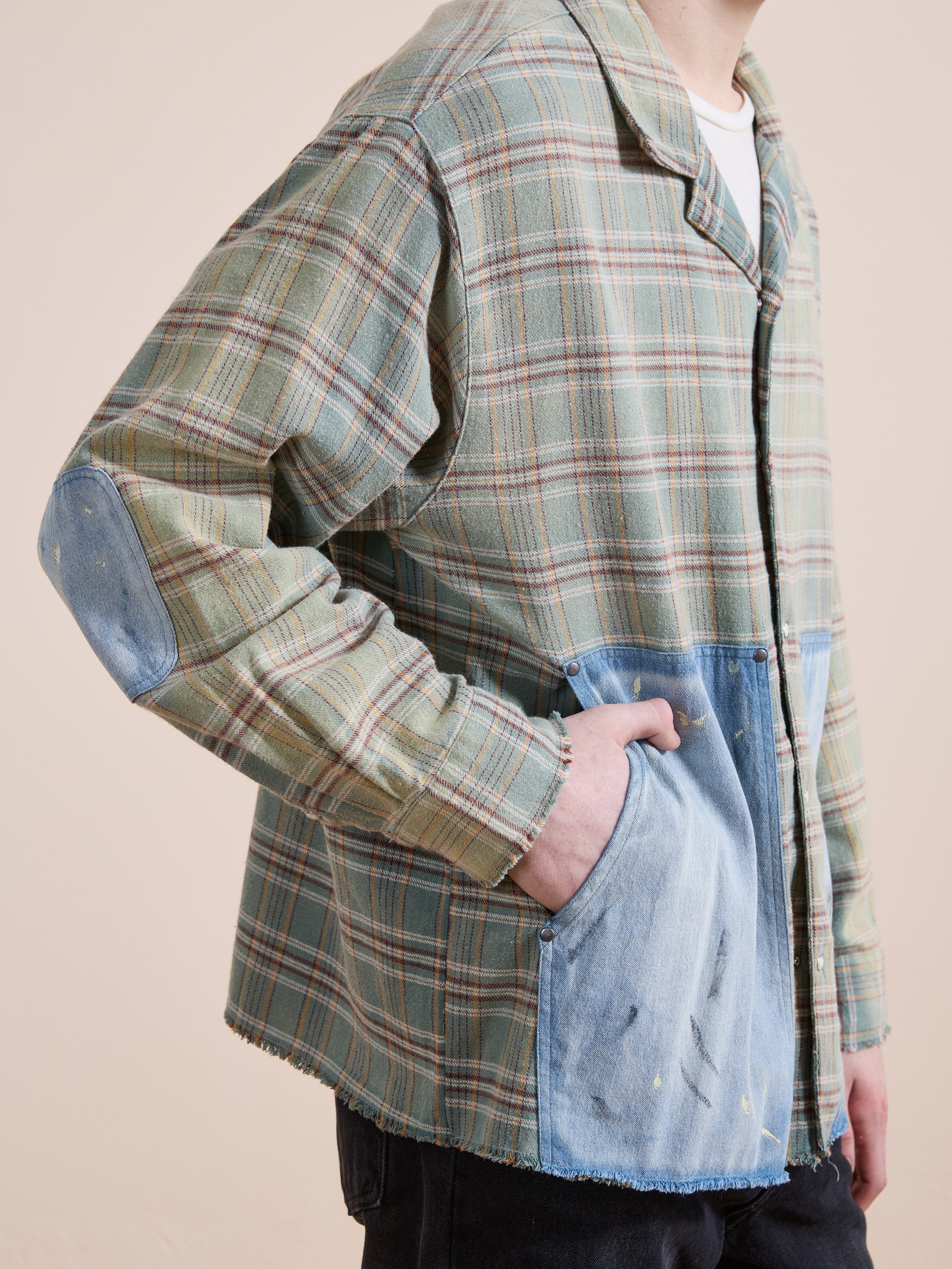 A person in the FOUND Plaid Denim Shirt, featuring carpenter pockets and elbow patches, stands with one hand in a pocket against a plain background—the perfect unisex workwear style.