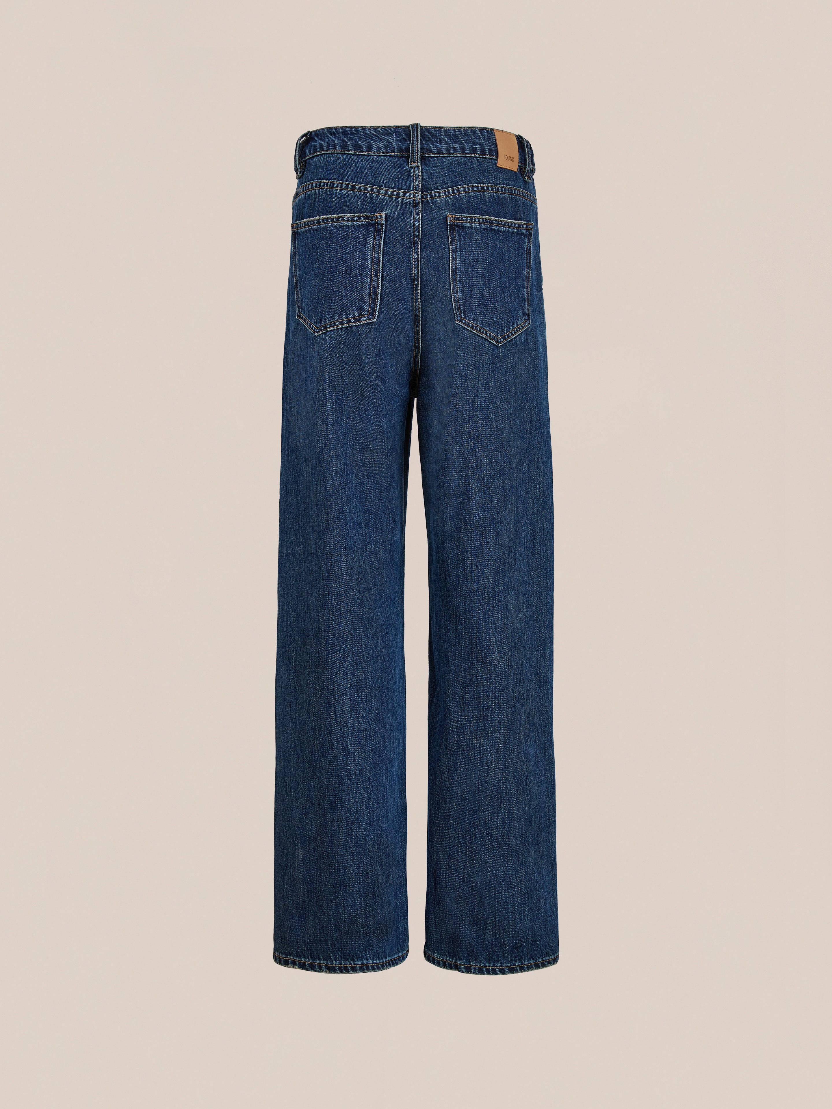 Back view of Found Pleated Relaxed Fit Jeans featuring two back pockets and a brown leather patch on the waistband, showcased against a plain light background.