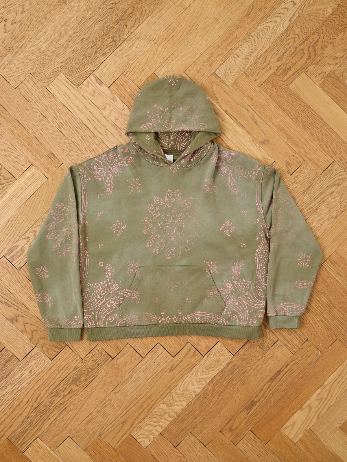 FOUND Printed Paisley Hoodie in olive green with pink paisley and floral print, shown laid flat on a light brown herringbone wood floor.