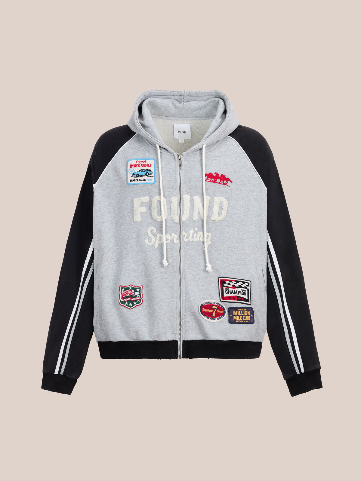 FOUND Racer Hoodie in gray and black with front pockets and colorful “FOUND Sporting” patches, shown on a plain beige background.