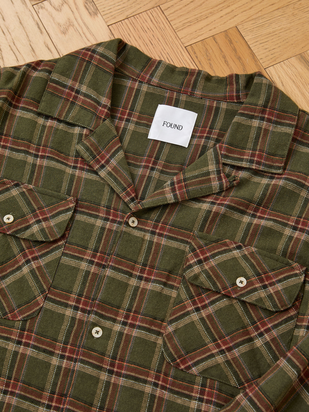 Green and red Raw Cut Fringe Plaid Camp Shirt by FOUND, featuring two chest pockets, laid flat on a light wood floor.