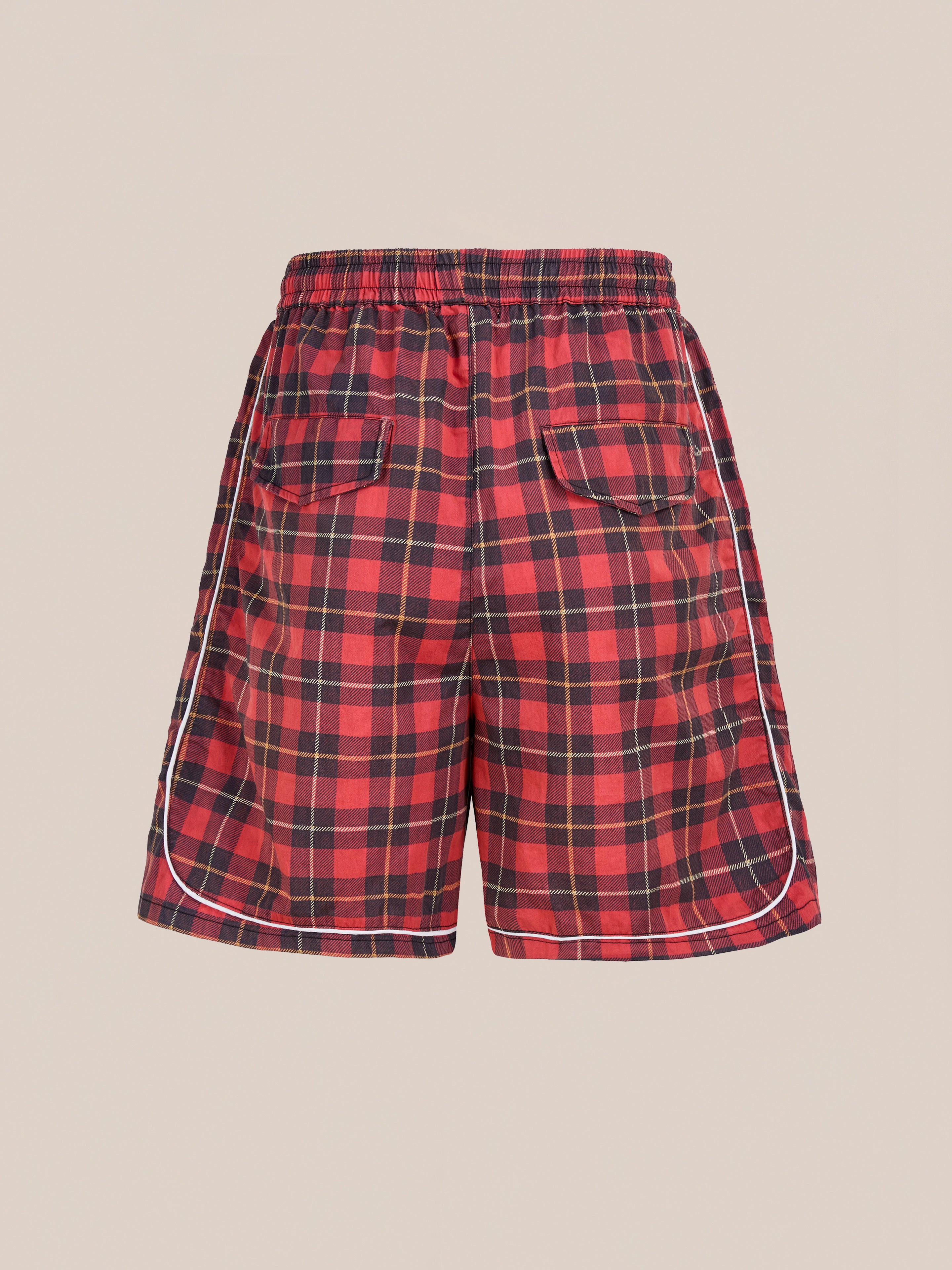Found Red Plaid Track Shorts feature black and red plaid design with white piping, elastic waistband, two back pockets, and a unisex relaxed fit for a vintage athletic look—all shown against a plain beige background.