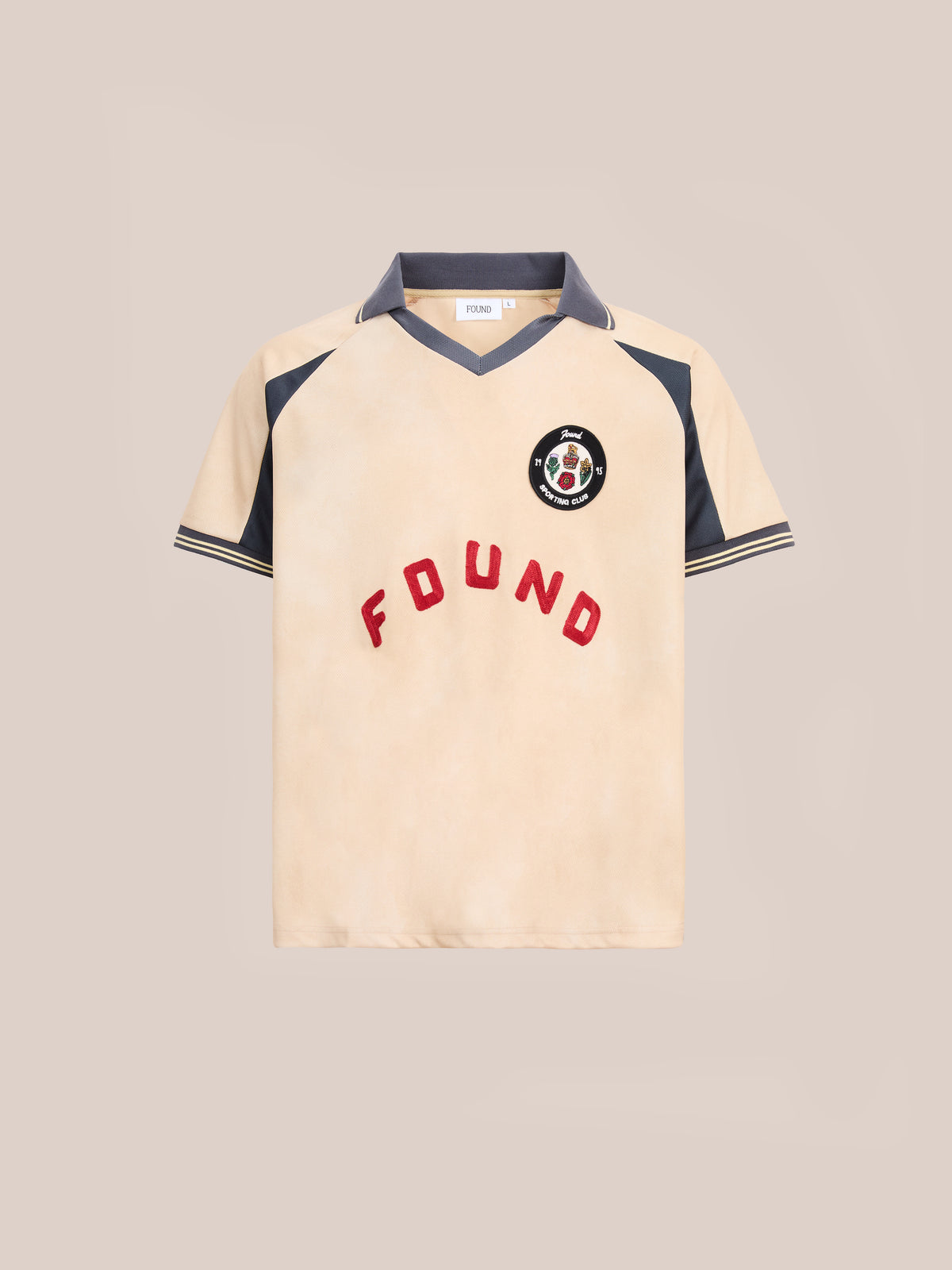 The Rosewood Jersey by FOUND is a short-sleeved beige shirt featuring dark gray collar and sleeve accents, vibrant red “FOUND” lettering, and a circular patch logo on the left chest—this unisex sportswear piece channels the timeless style of a vintage football jersey.