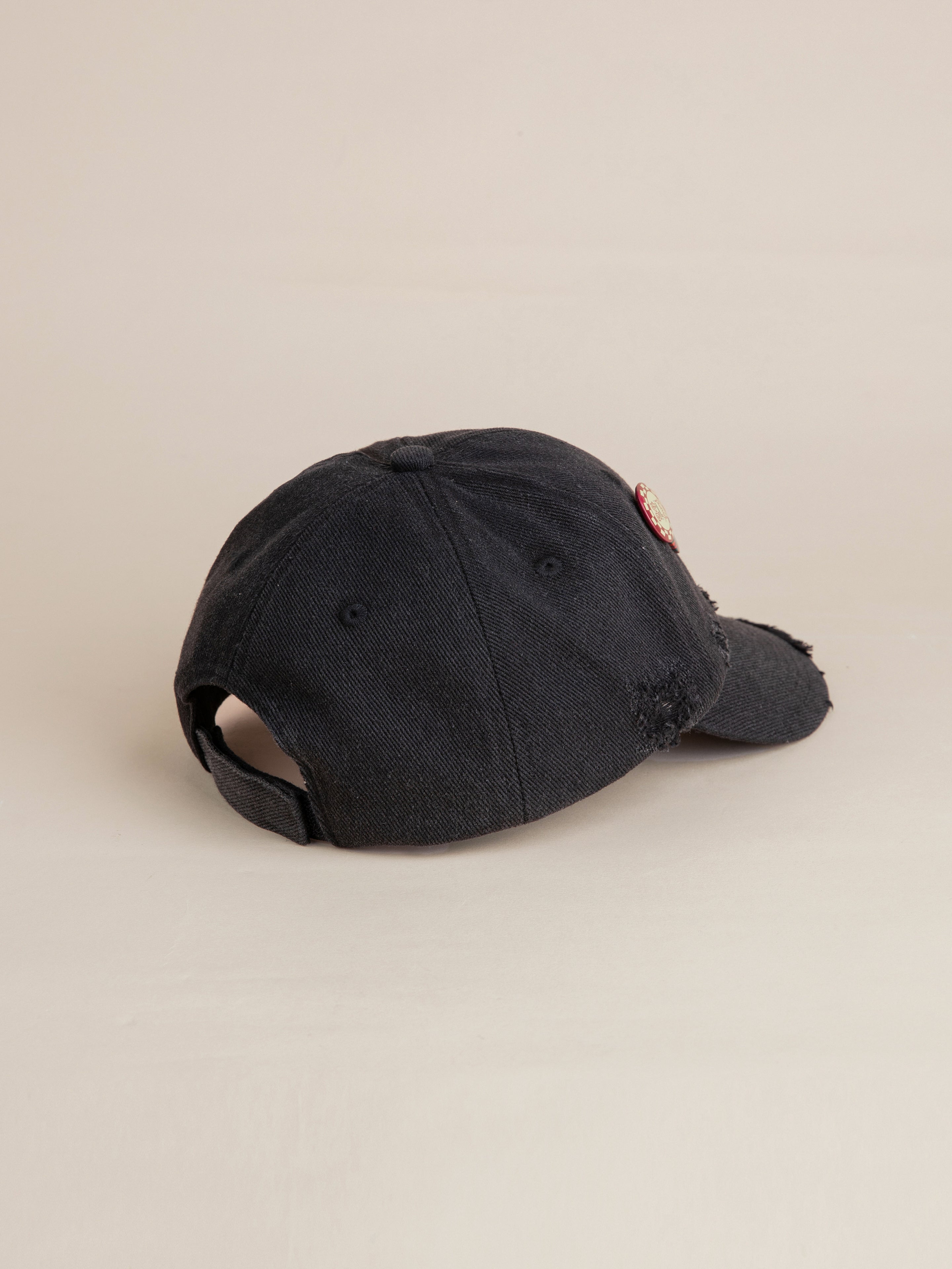 The Distressed Pin Cap by FOUND, featuring a curved brim and an adjustable strap in the back, is a black cotton cap adorned with vintage-inspired pins and displayed on a neutral background.