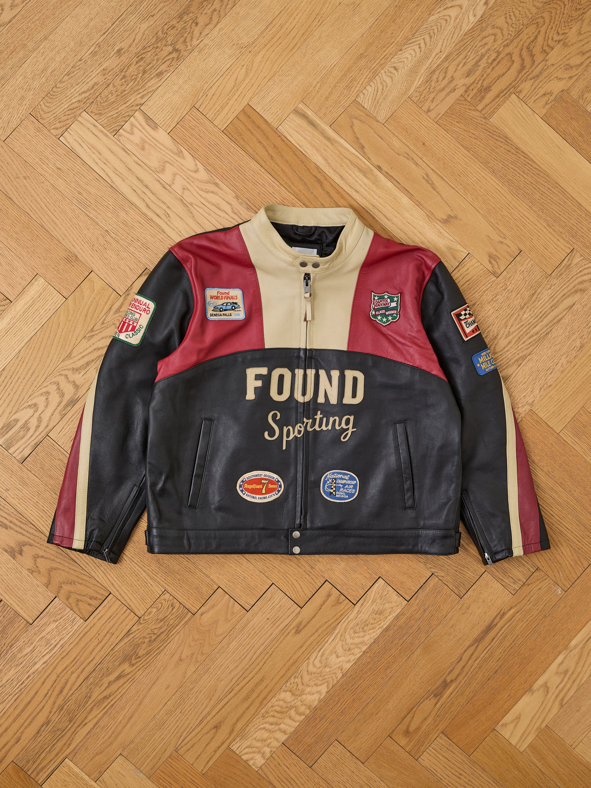 FOUND Sport Racer Jacket—color-blocked cowhide with “FOUND Sporting” text and embroidered patches, displayed on a wooden herringbone floor.