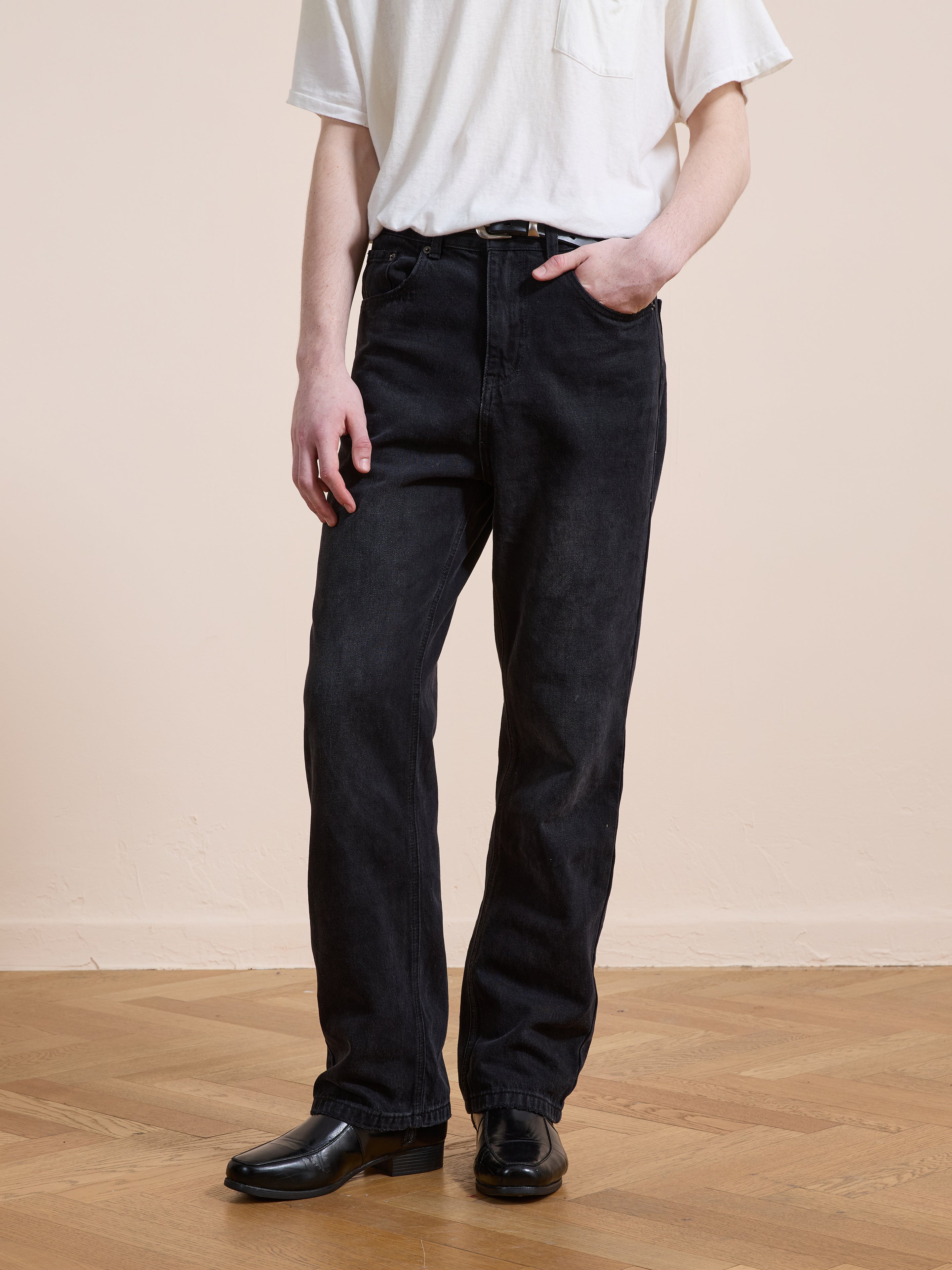 Someone wearing Found Straight Leg Jeans with a white short-sleeve t-shirt, belt, and black shoes stands on a wooden floor against a neutral background.