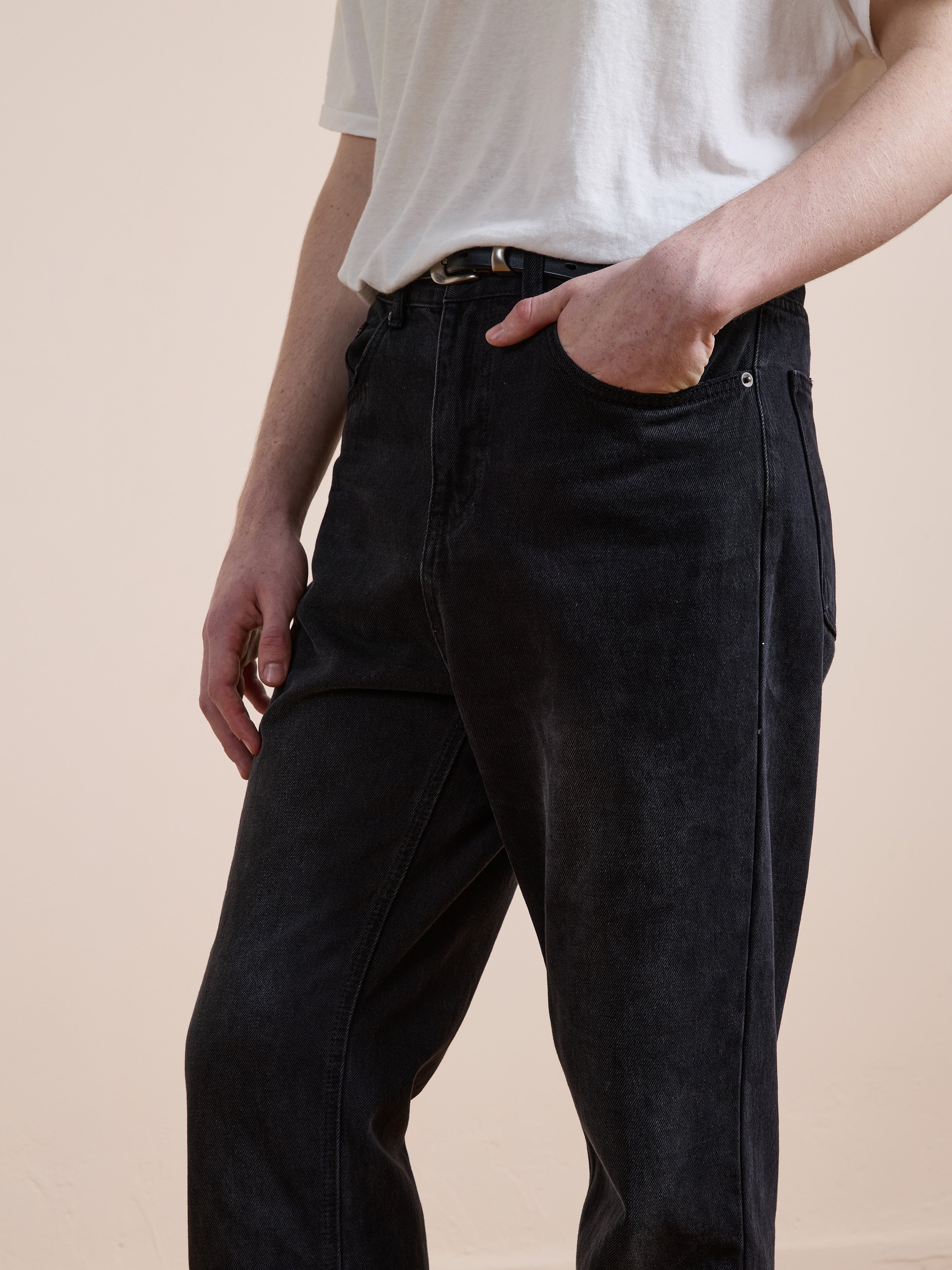 A person wears Found Straight Leg Jeans, high-waisted and classic denim, paired with a white t-shirt tucked in; one hand is in the pocket while the other rests by their side.