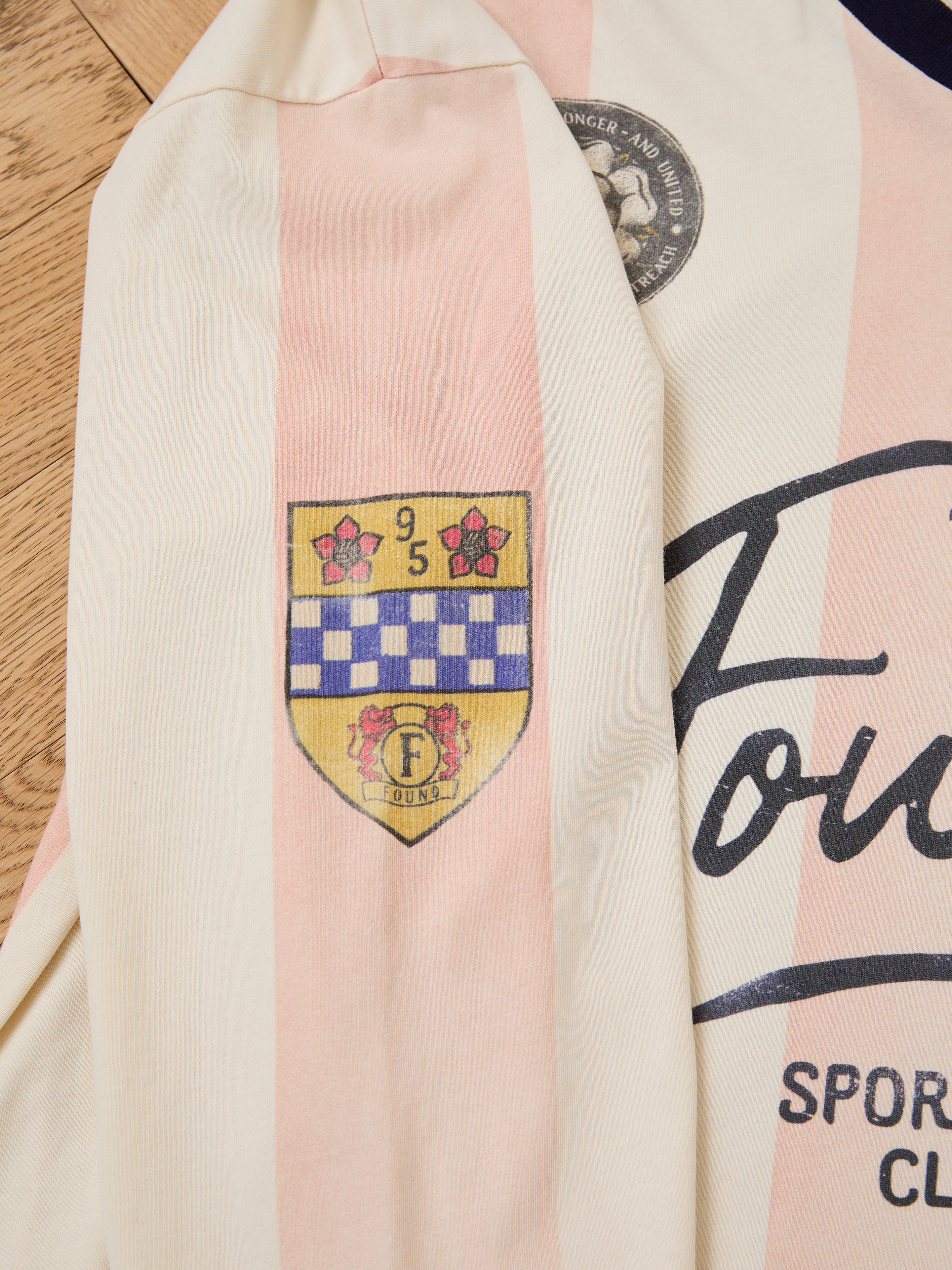 A close-up of the FOUND Striped Sport LS Jersey sleeve shows cream and pink stripes with a yellow and blue crest displaying flowers, numbers, and an "F" above the word "Touré.