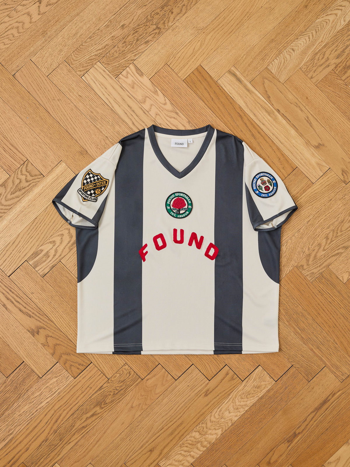 The Striped Stateman Jersey by FOUND features black and white stripes, bold red “FOUND” text, embroidered patches—a unisex sportswear standout.