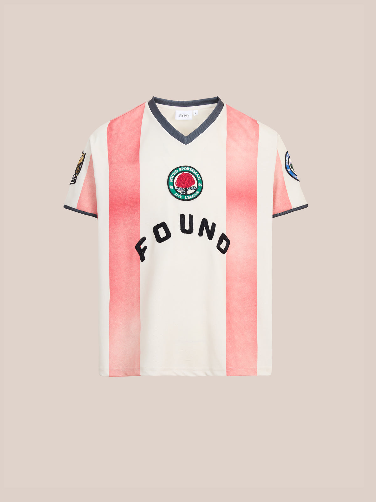 The Striped Stateman Jersey by FOUND is a short-sleeve shirt featuring white and pink vertical stripes, vintage football jersey-inspired details, “FOUND” lettering and a round patch logo on the chest, shown against a plain beige background.