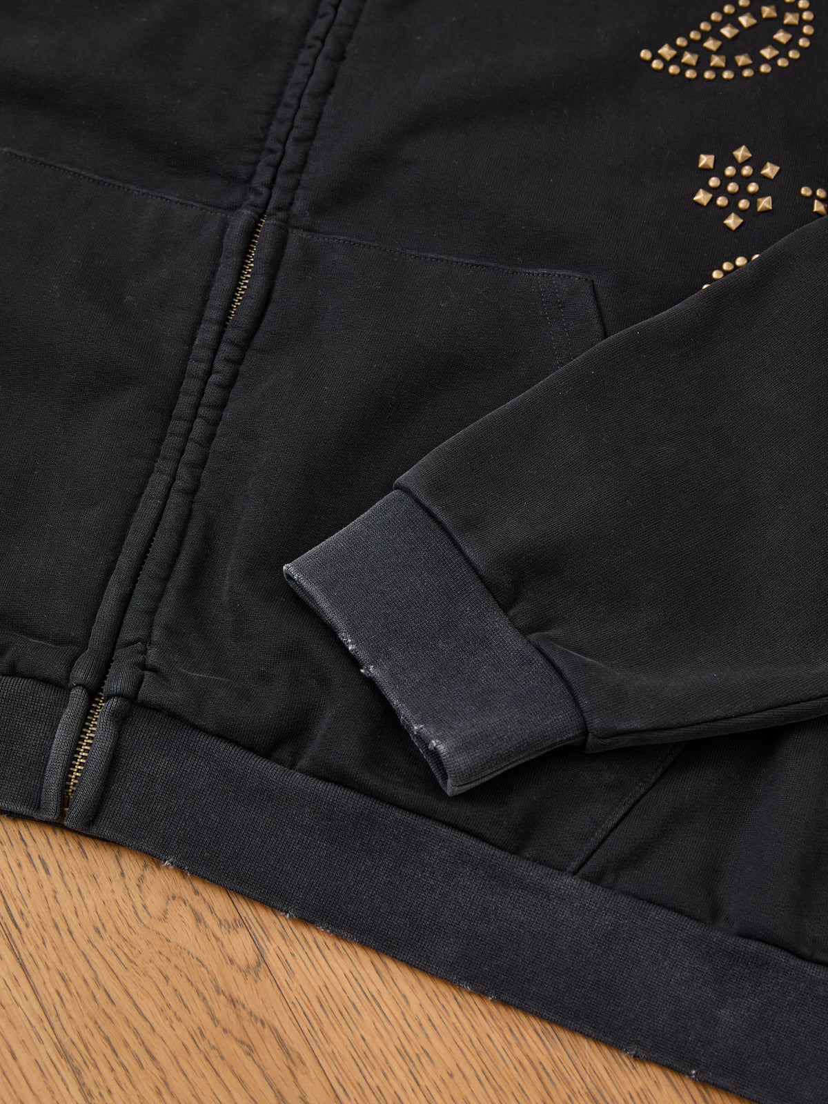 FOUND Studded Zip Up Hoodie with gold studs and worn sleeve cuff, displayed on wood for a cool vintage look.