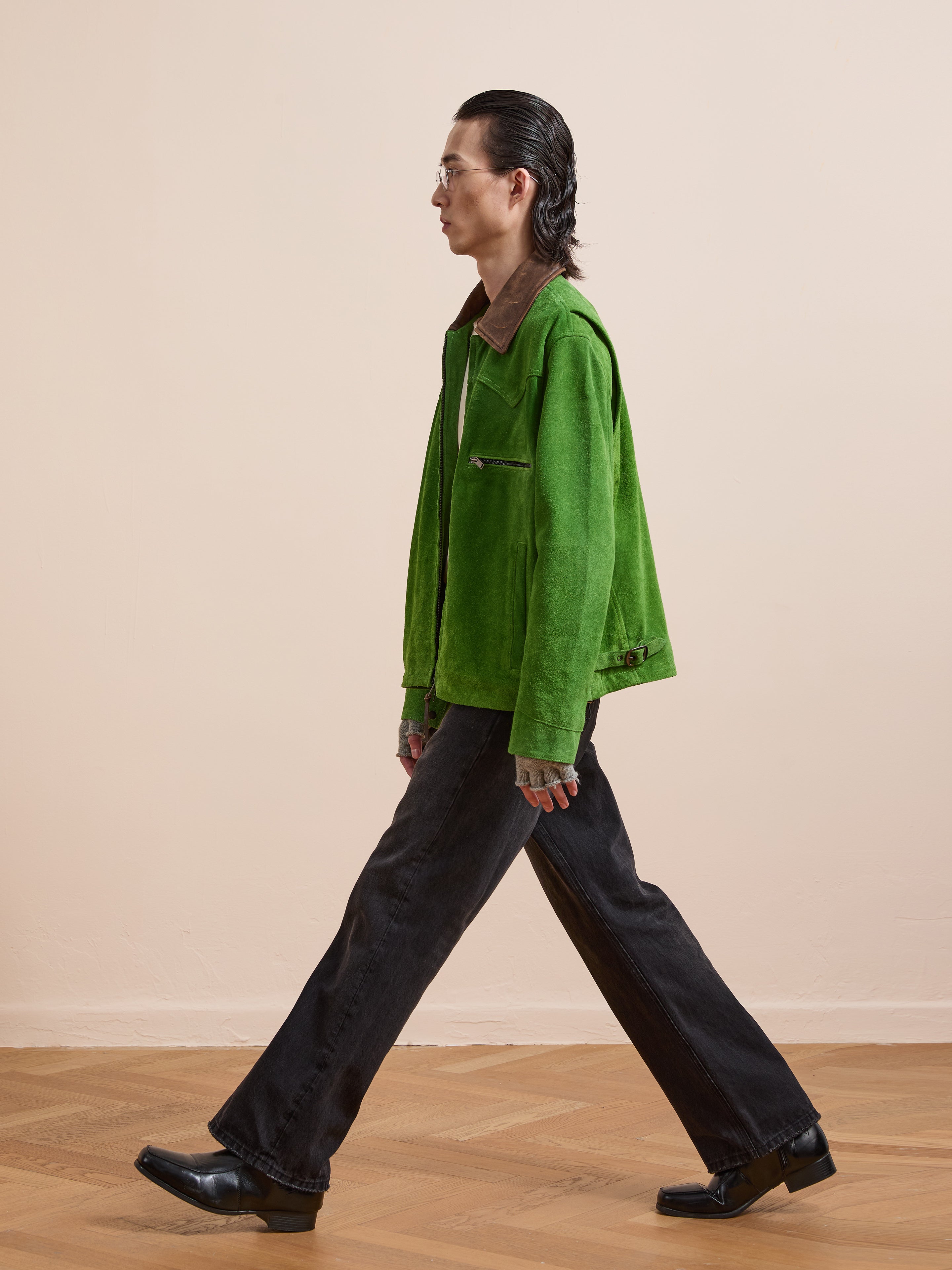 A person in the FOUND Suede Western Barn Jacket, black pants, and black shoes walks left on a wooden floor against a plain light wall.