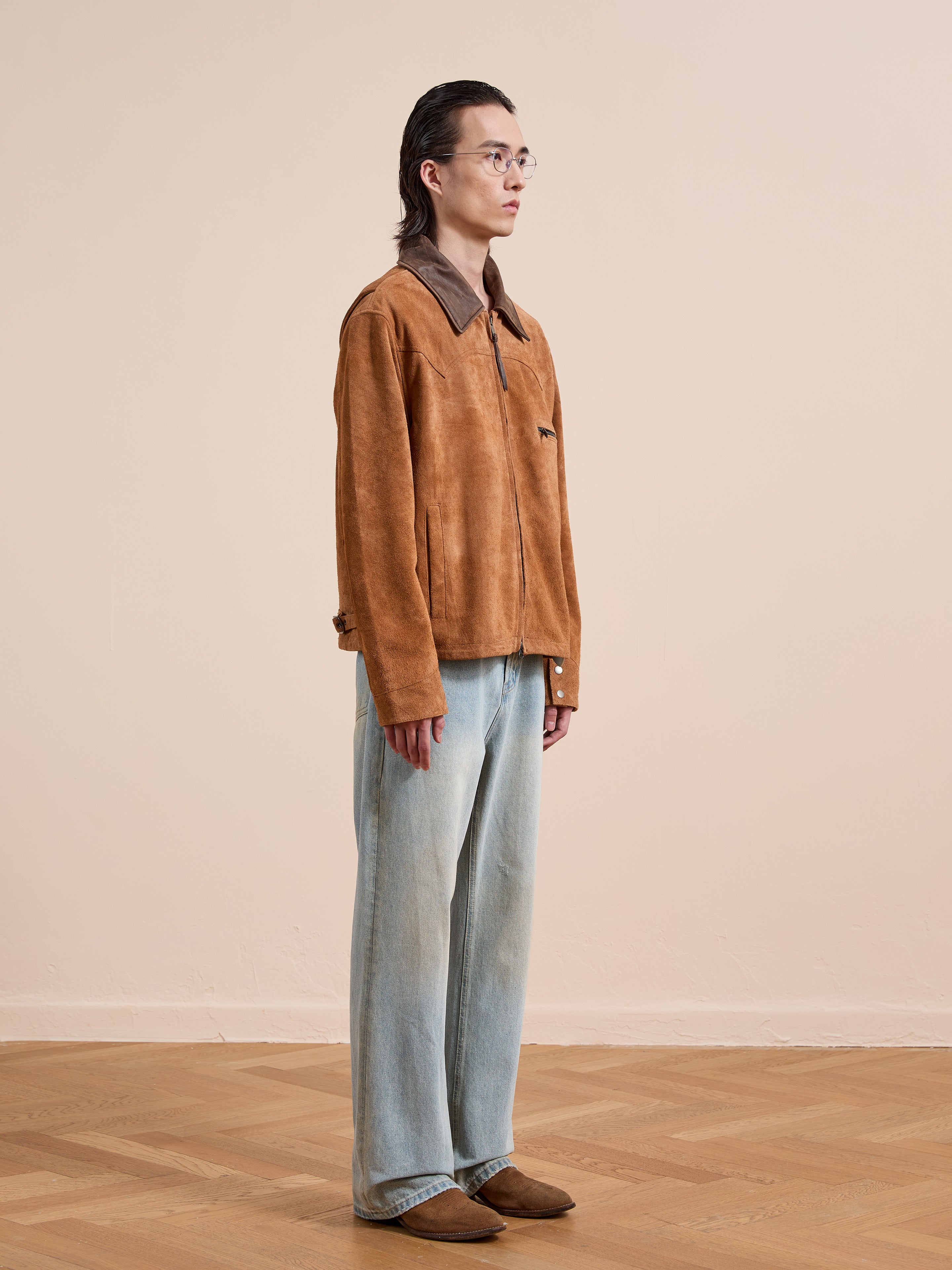 A person stands indoors wearing the FOUND Suede Western Barn Jacket, light blue jeans, brown shoes, and glasses against a plain beige background.