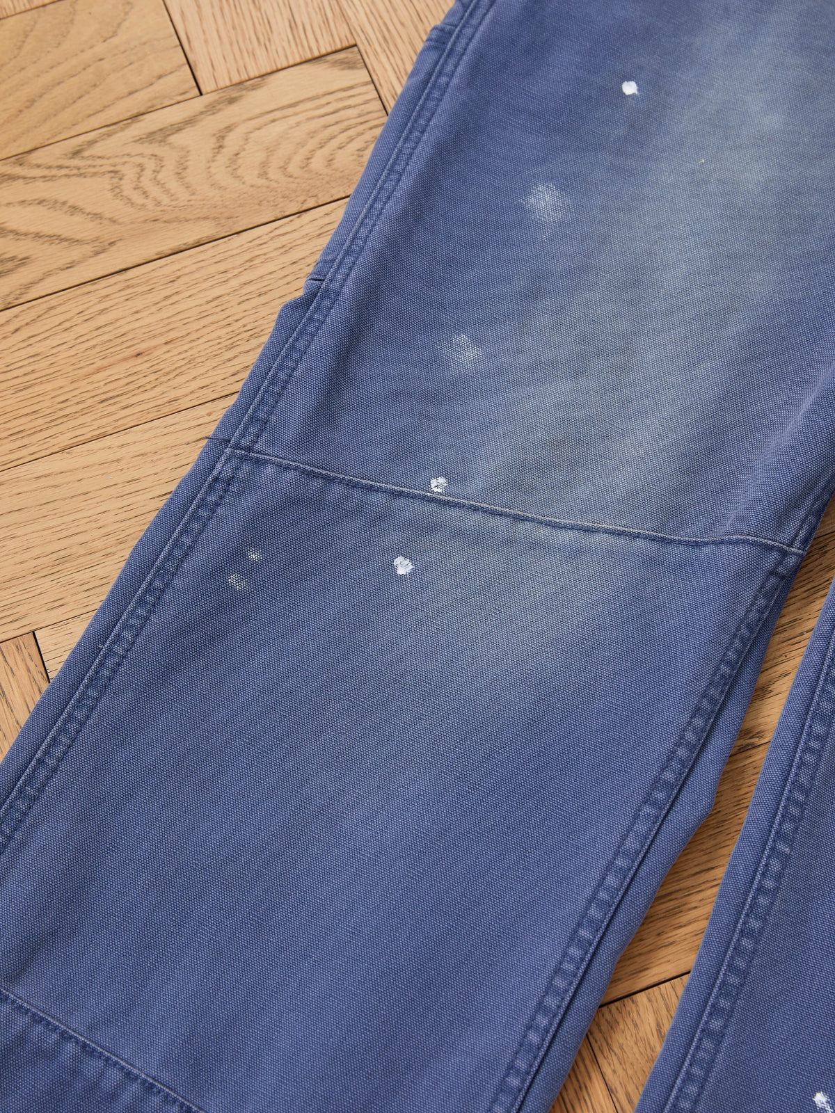 FOUND Sunbleached Utility Pants, relaxed fit with visible fading and small white stains, shown laid flat on a light wood floor.