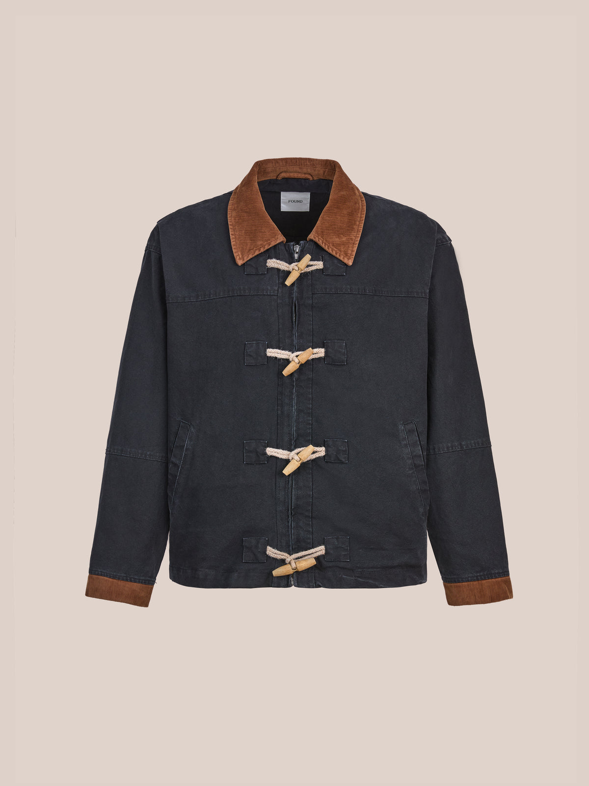 The Found Toggle Work Jacket features dark denim, a brown corduroy collar and cuffs, and fireman-style front closure with four wooden toggles, reimagining the vintage work jacket in a unisex relaxed fit. Displayed on a plain background.