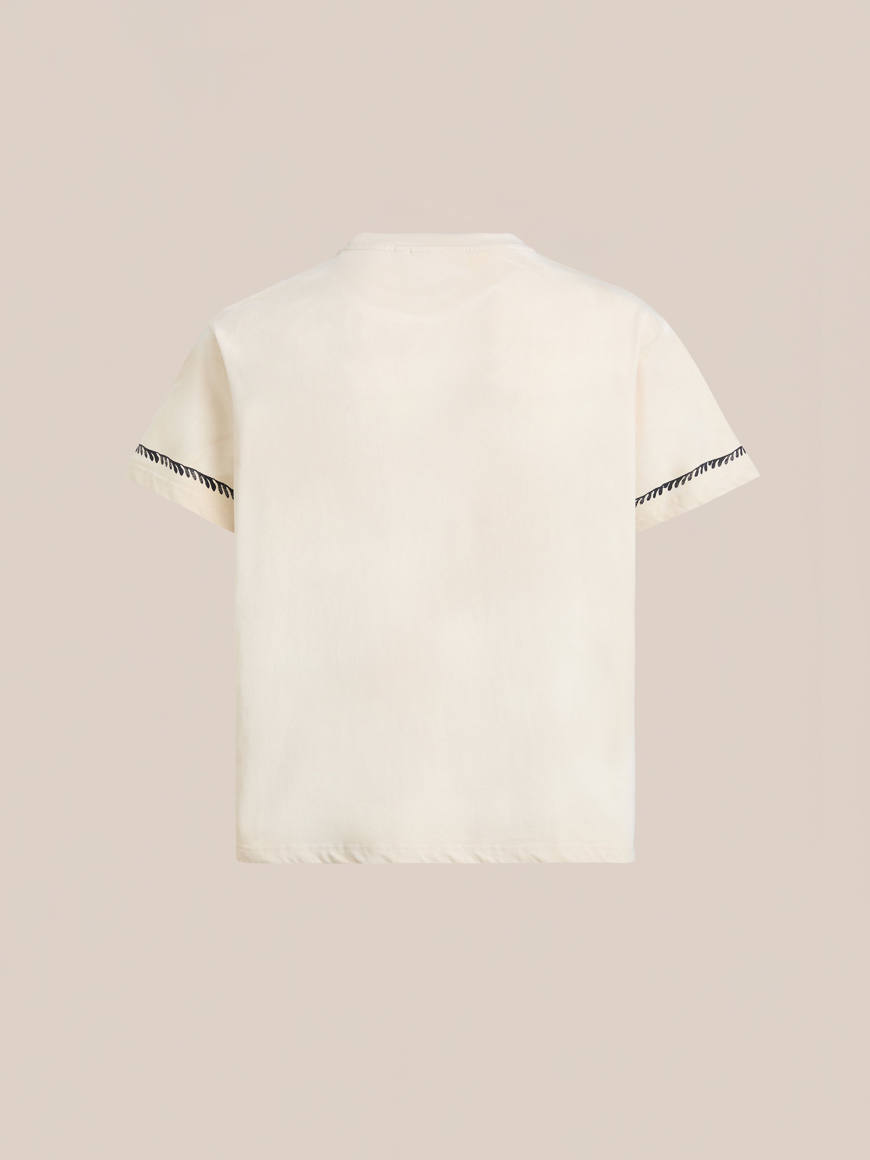 The Unity Crest Tee by FOUND is a cream short-sleeve t-shirt shown from the back, made from mid-weight cotton and featuring black zigzag detailing on the sleeve hems.