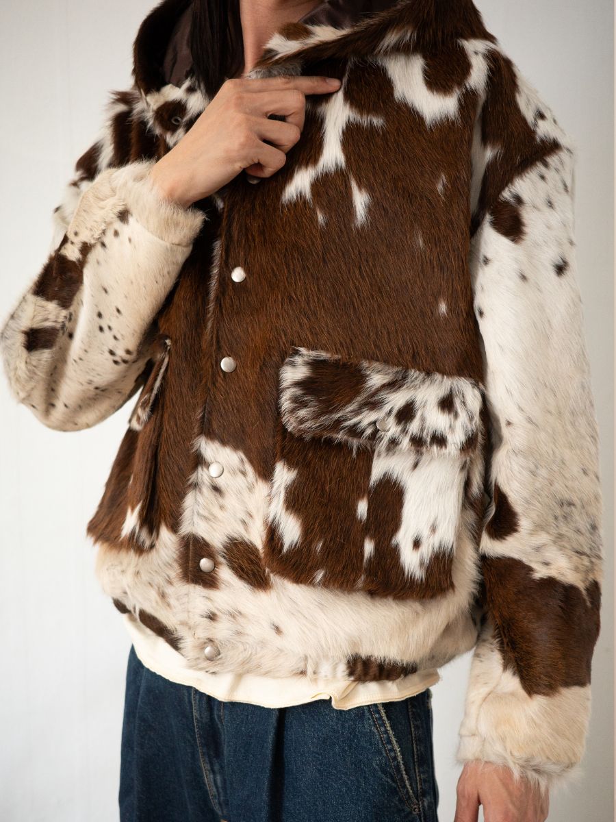 Wearing the FOUND Cowhide Drover Hoodie—crafted from genuine cowhide with snap buttons—and blue jeans, this person stands against a plain background. The unisex relaxed fit ensures comfort and timeless style.