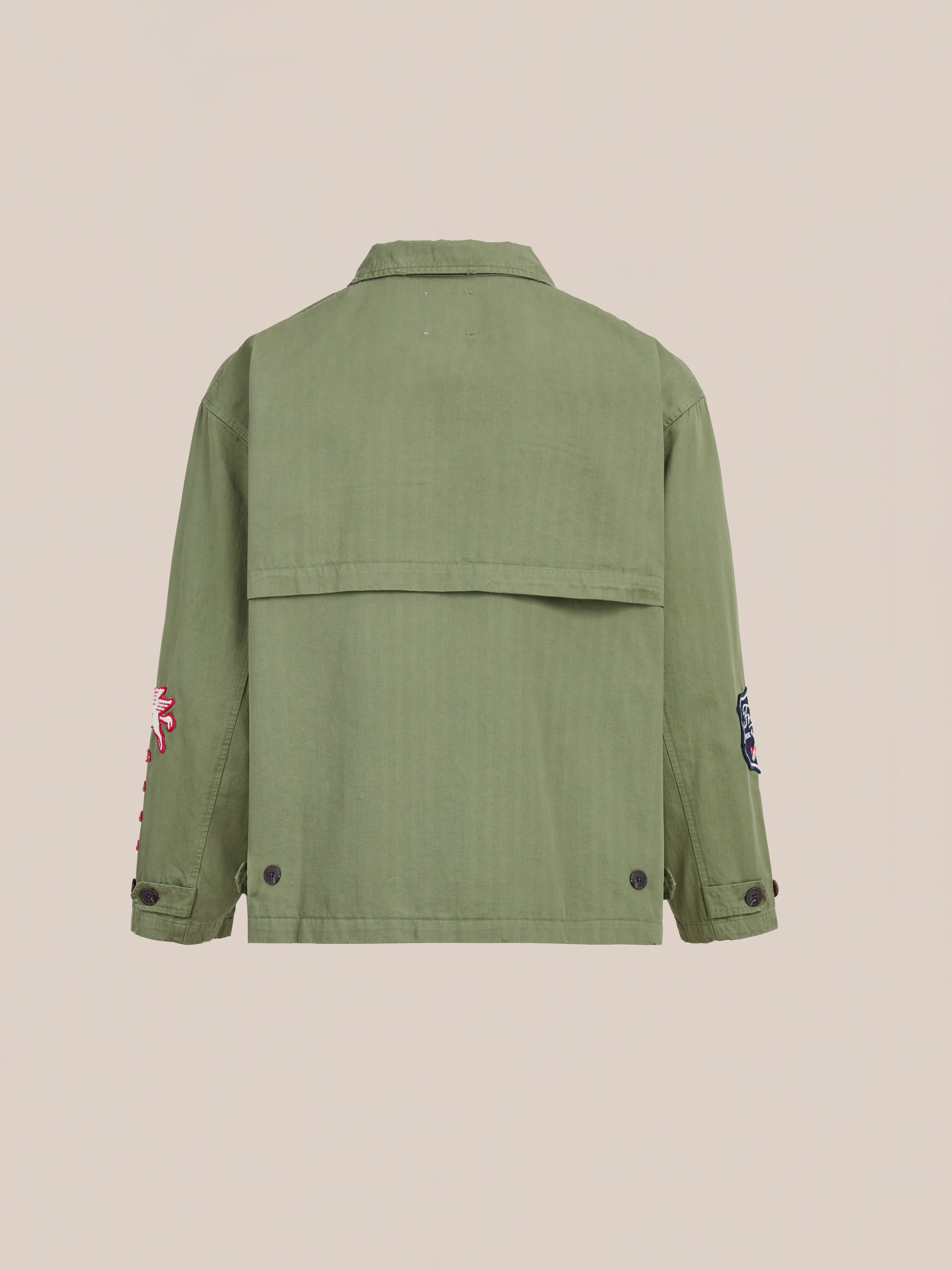 The FOUND Herringbone Utility Patchwork Jacket is shown from the back, featuring buttoned cuffs and hem, with embroidered sleeve patches and crafted from durable cotton herringbone.