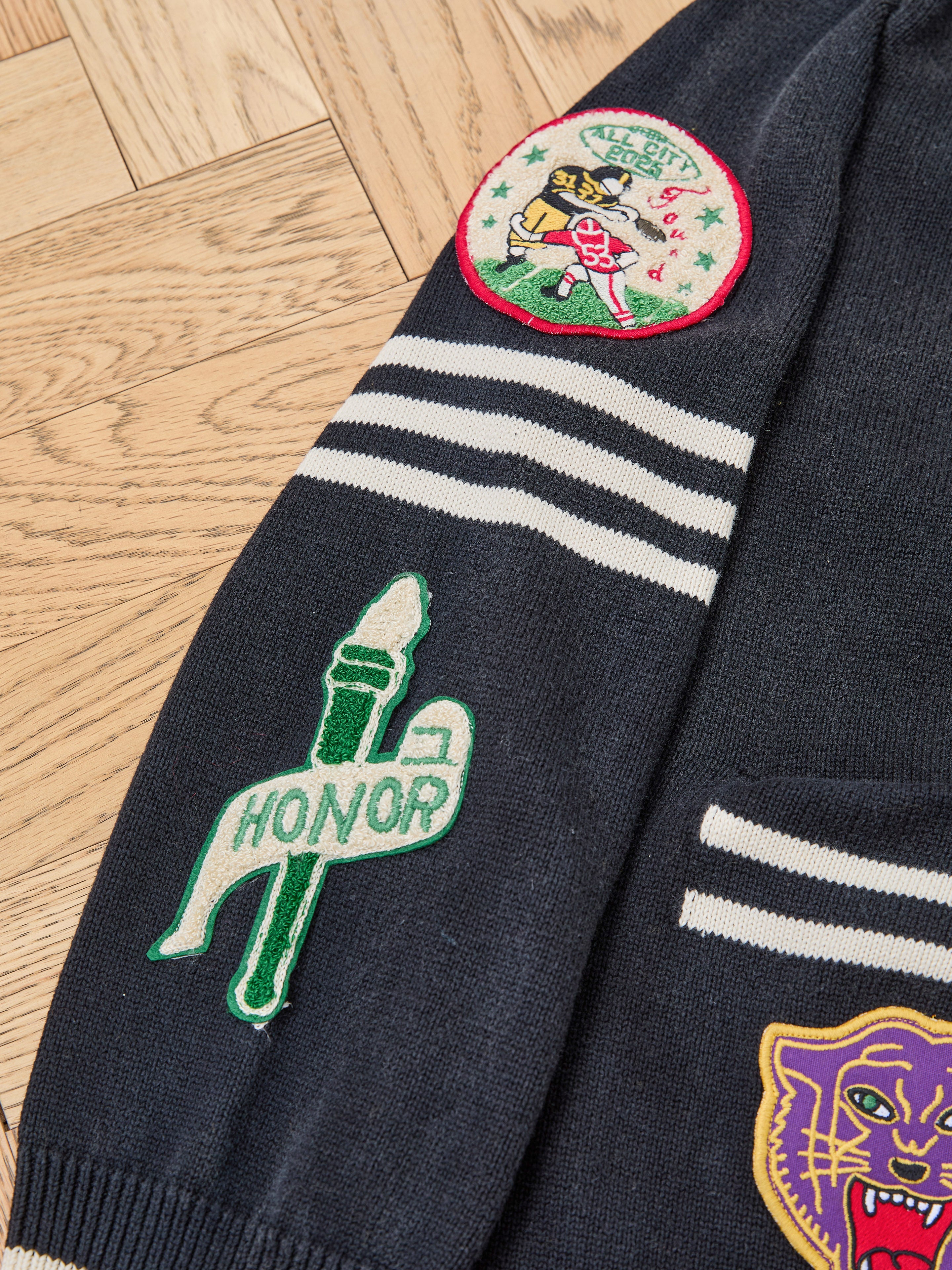 The FOUND Varsity Patch Collared Cardigan features soft dark blue cotton knit with white sleeve stripes and three chenille patches: a "HONOR" torch, cat face, and circular bear mascot reading "LUCKY SEVEN.