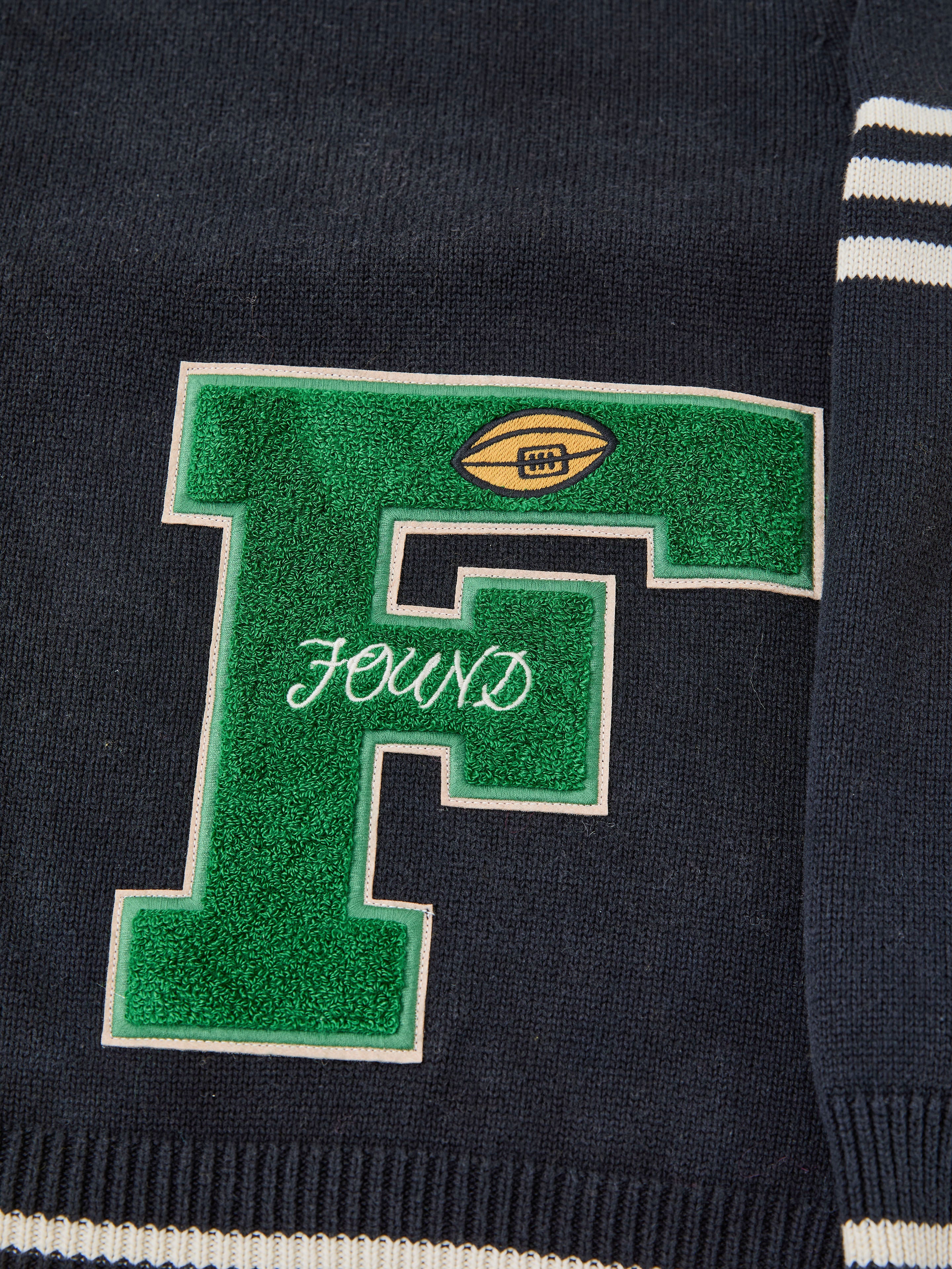 The FOUND Varsity Patch Collared Cardigan is a dark blue cotton knit with a large green chenille "F," a small football graphic, and "FOUND" stitched in white.