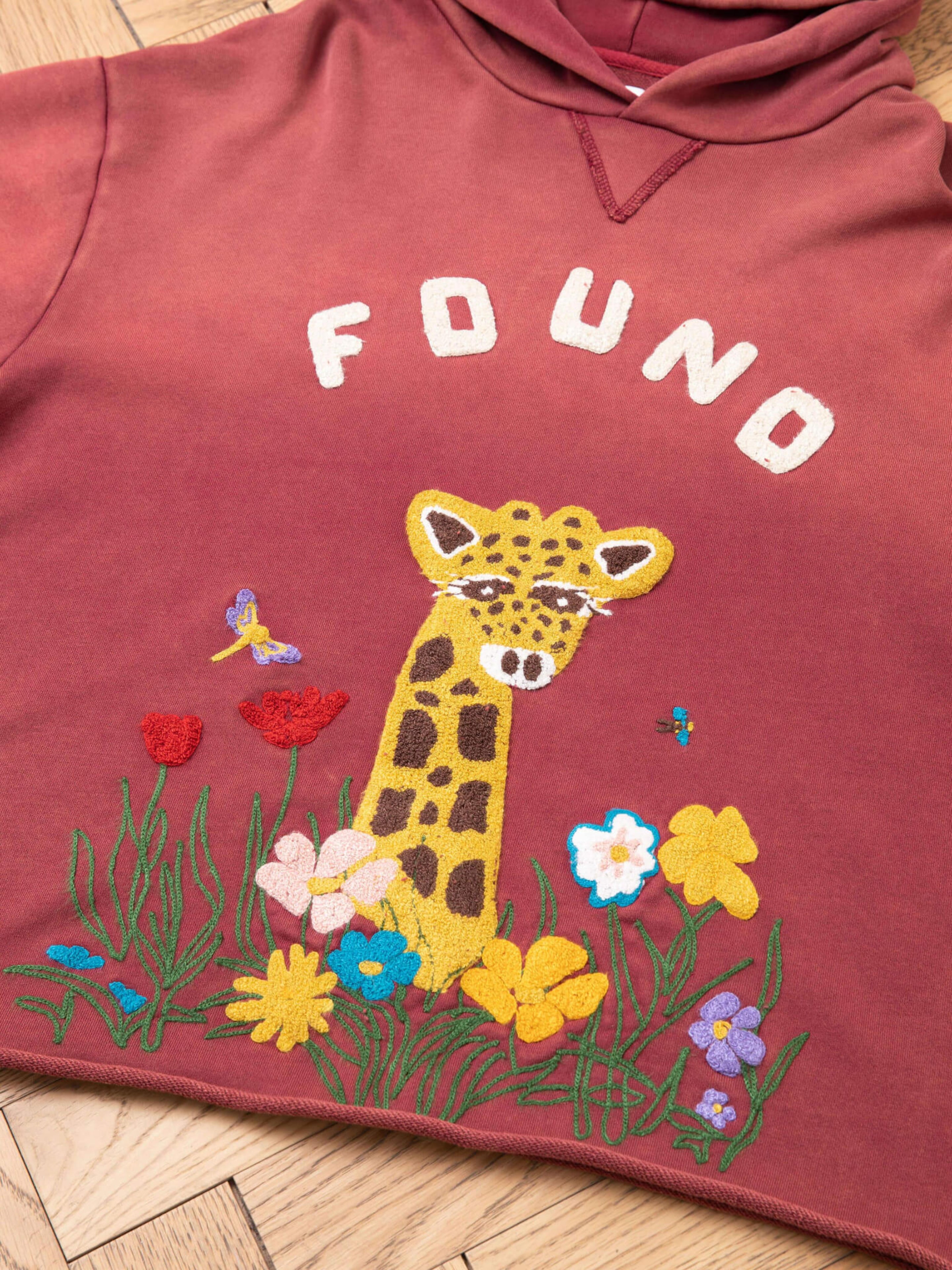 The FOUND Embroidered Wildlife Hoodie in maroon features chenille embroidery of a giraffe, flowers, butterfly, and bee on the front with "FOUND" text.