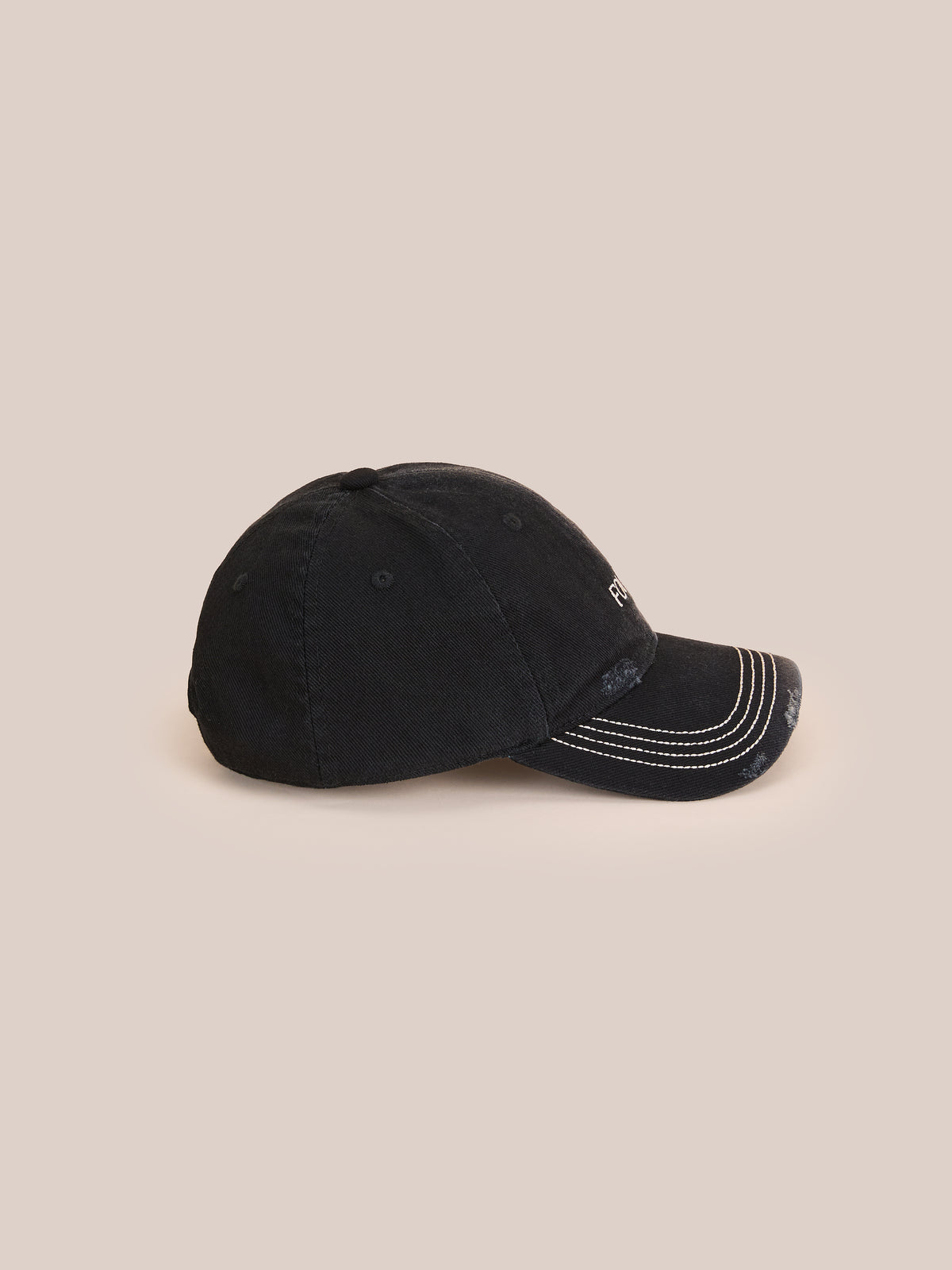 The Washed Logo Cap by Found is a black distressed baseball cap with white stitching and an adjustable leather strap, shown side view on a beige background.