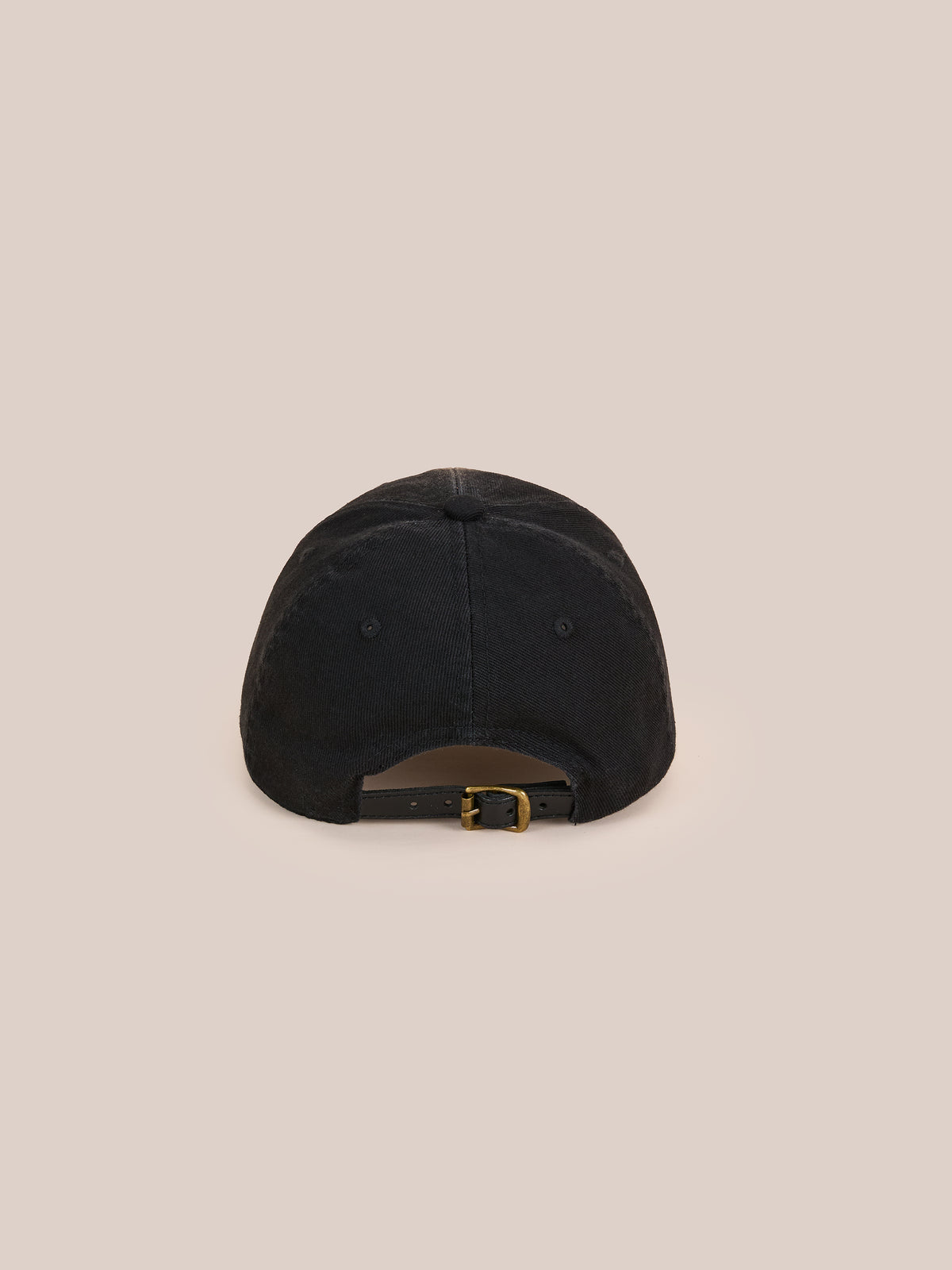 The Washed Logo Cap by Found, shown from the back, features a black distressed look and an adjustable brass buckle strap against a beige background.