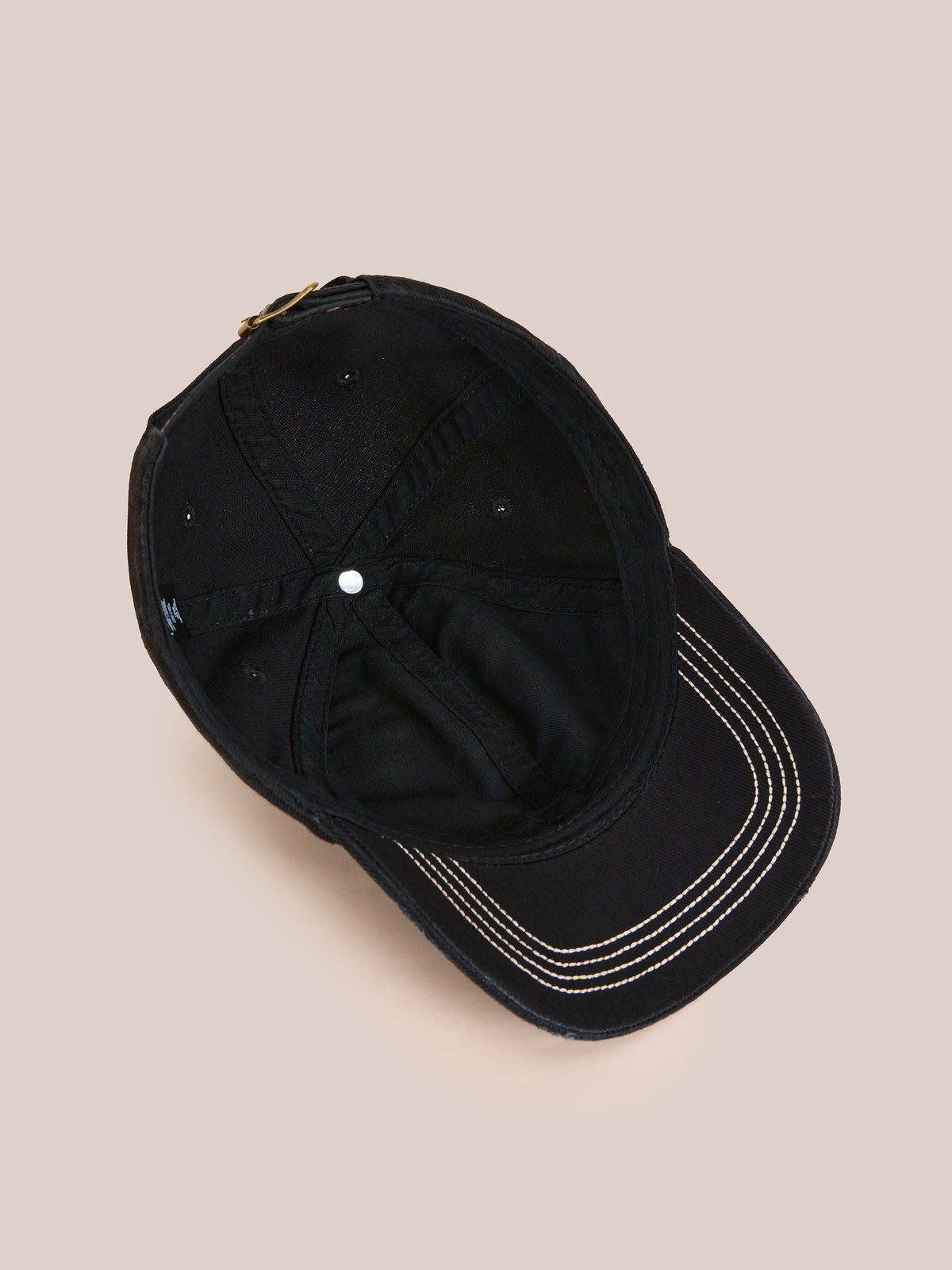 The Washed Logo Cap by Found, a distressed black hat with white-stitched brim and adjustable leather strap, is shown from above on a beige background.