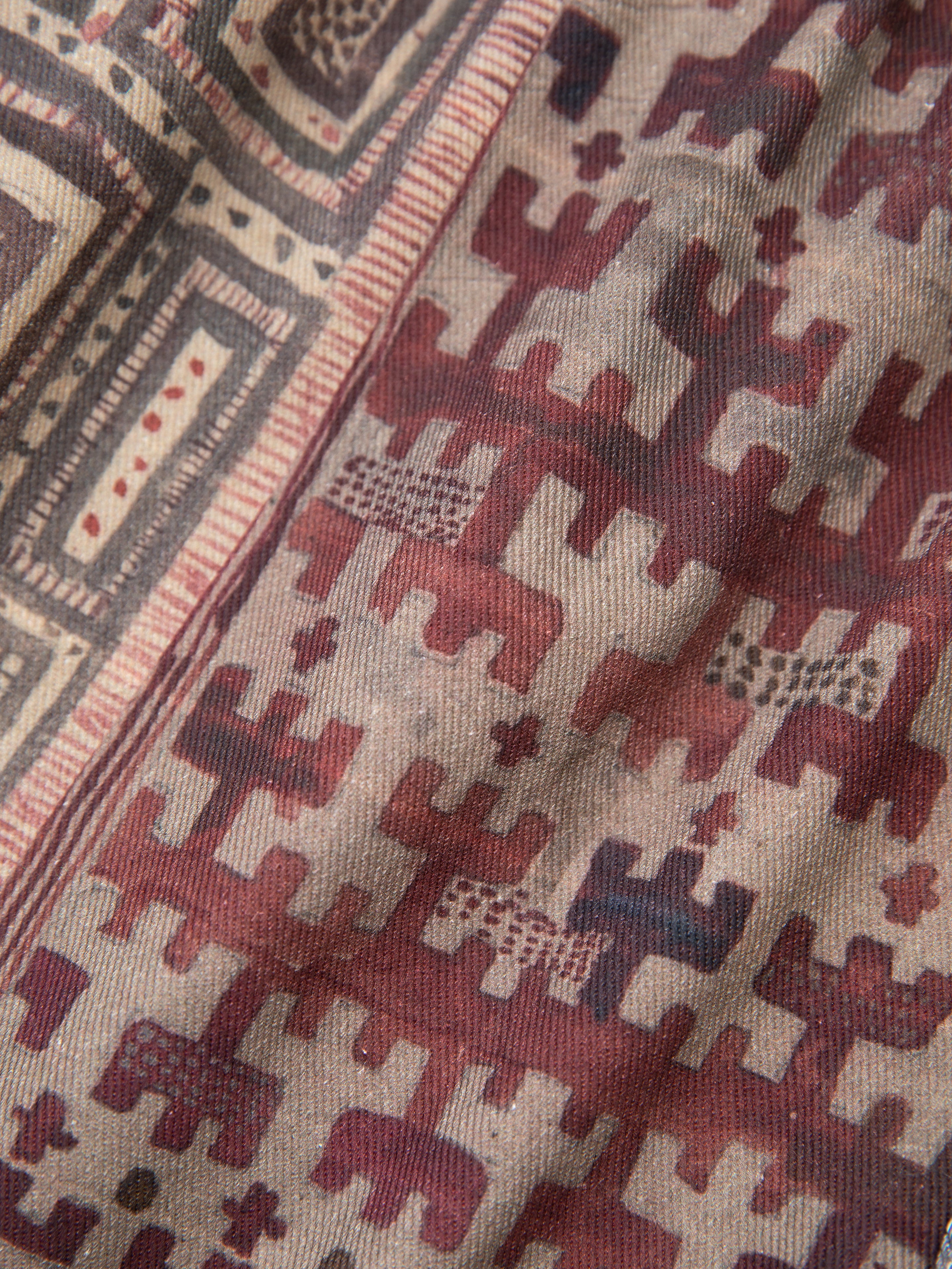 Close-up of a fabric with vintage-inspired geometric patterns in red, brown, and beige, featuring squares and abstract shapes reminiscent of watercolor mosaic. Perfect for creating unisex relaxed-fit garments like the FOUND Watercolor Mosaic Work Shorts.