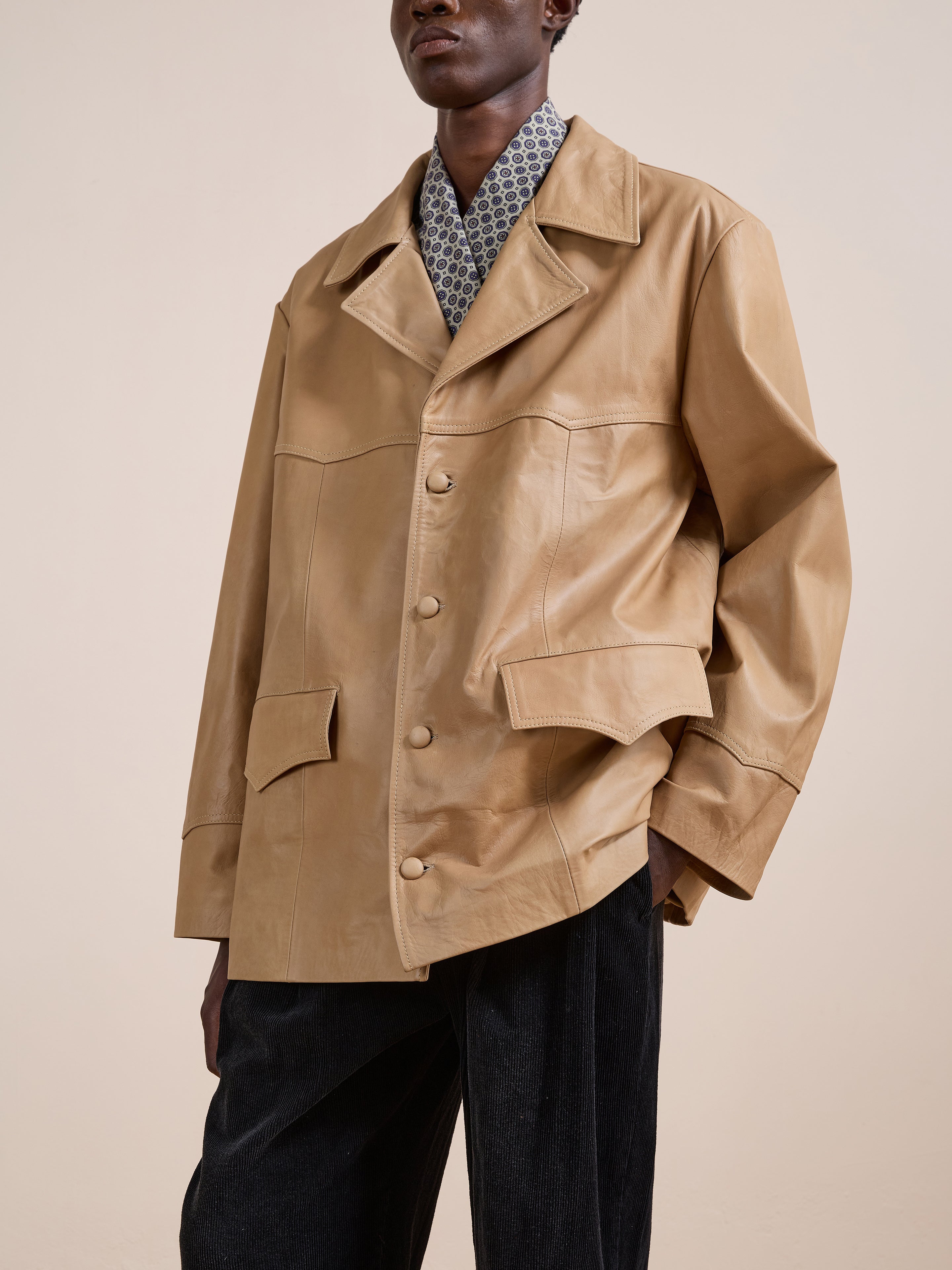 A person wearing the FOUND Western Oversized Leather Blazer in light brown, styled over a patterned shirt and dark pants, stands against a plain beige background.