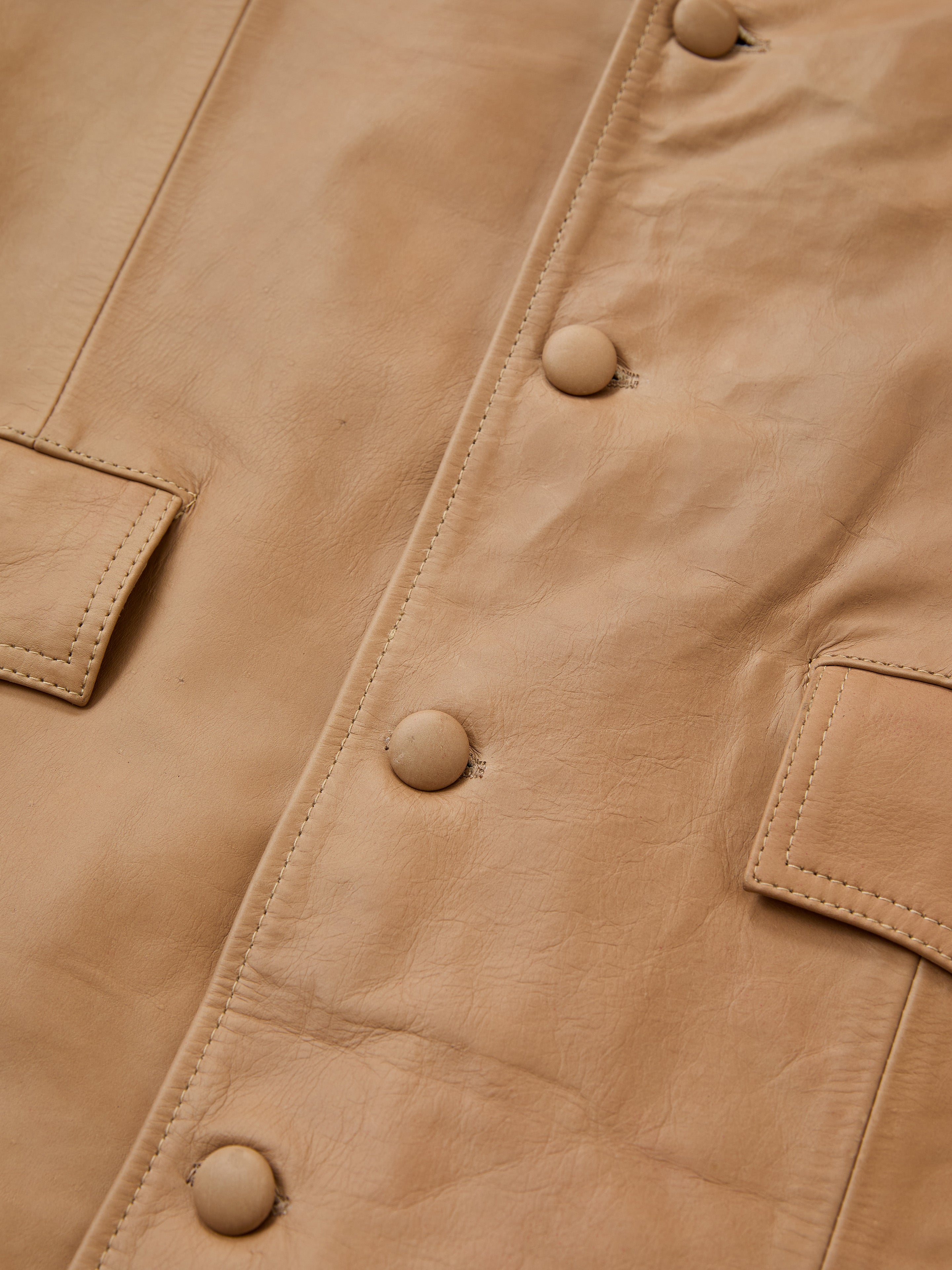 Close-up of the FOUND Western Oversized Leather Blazer in tan leather, showcasing round buttons and two front pockets with stitched flaps.