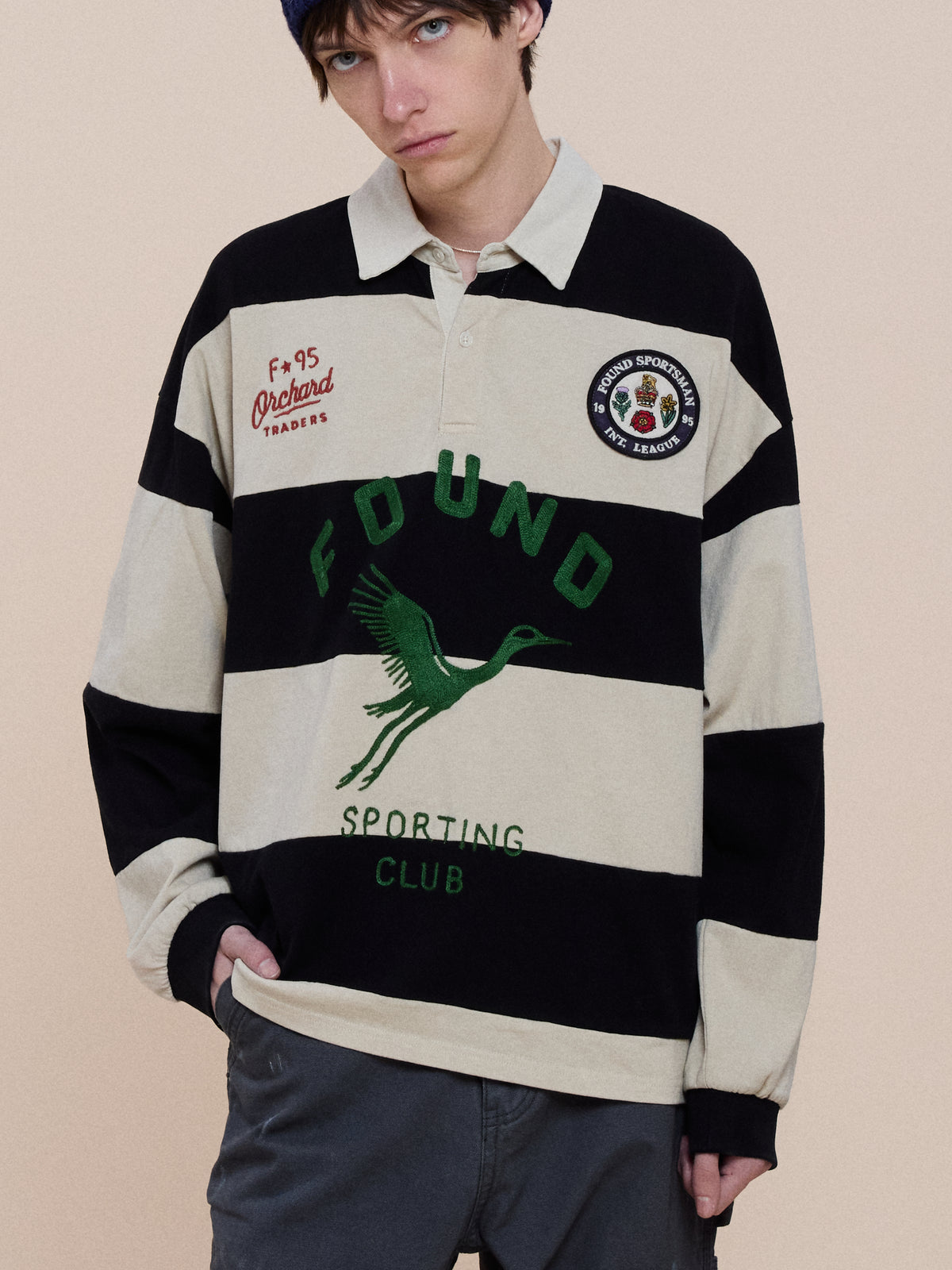 Person wearing a Bird Logo Rugby by FOUND, a black and cream striped unisex cotton top with crane logo, standing against a plain background.