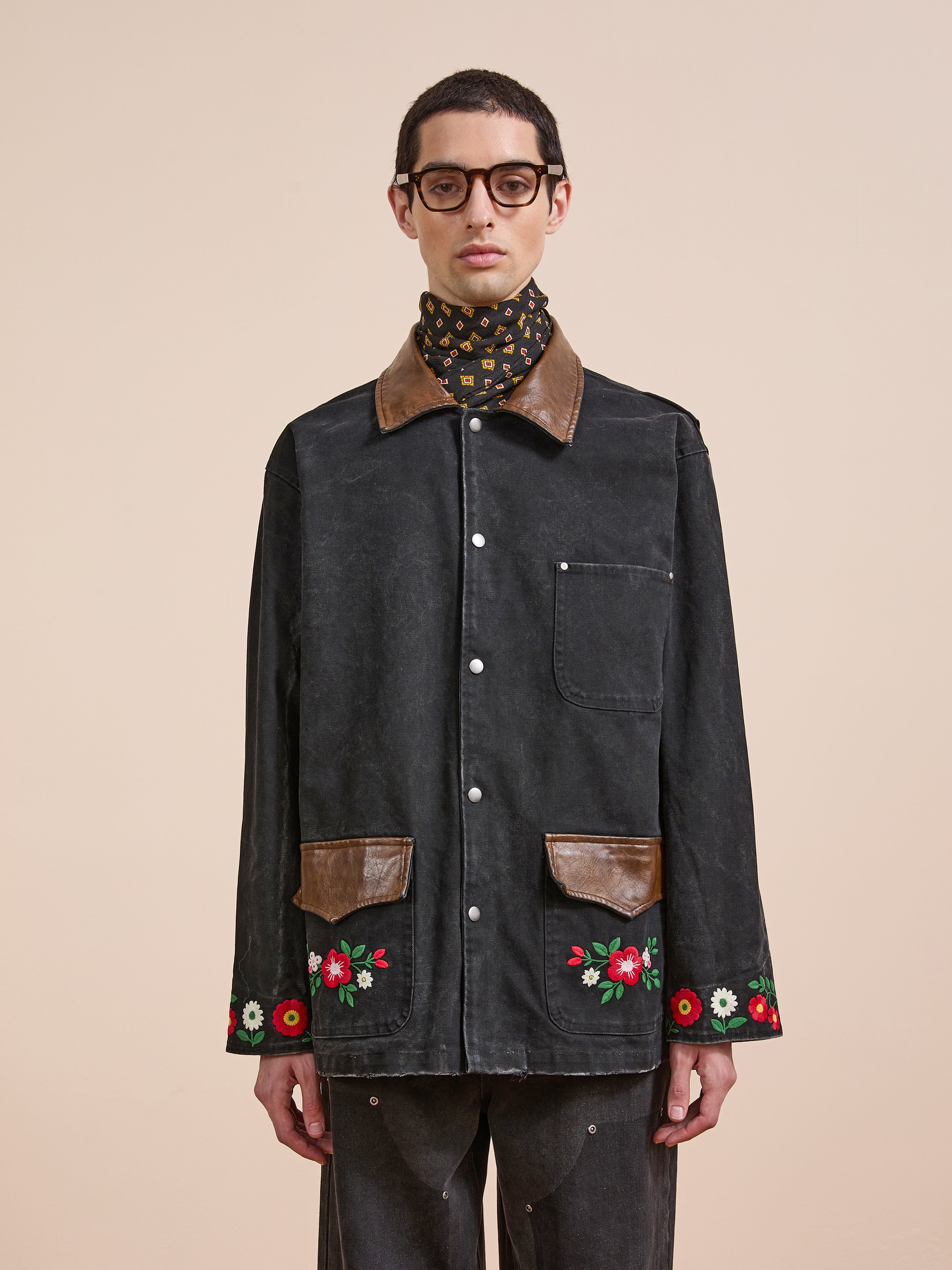 A man in the Found Canvas Embroidered Work Jacket, featuring brown accents and floral embroidery on the cuffs and pockets, stands against a beige background.