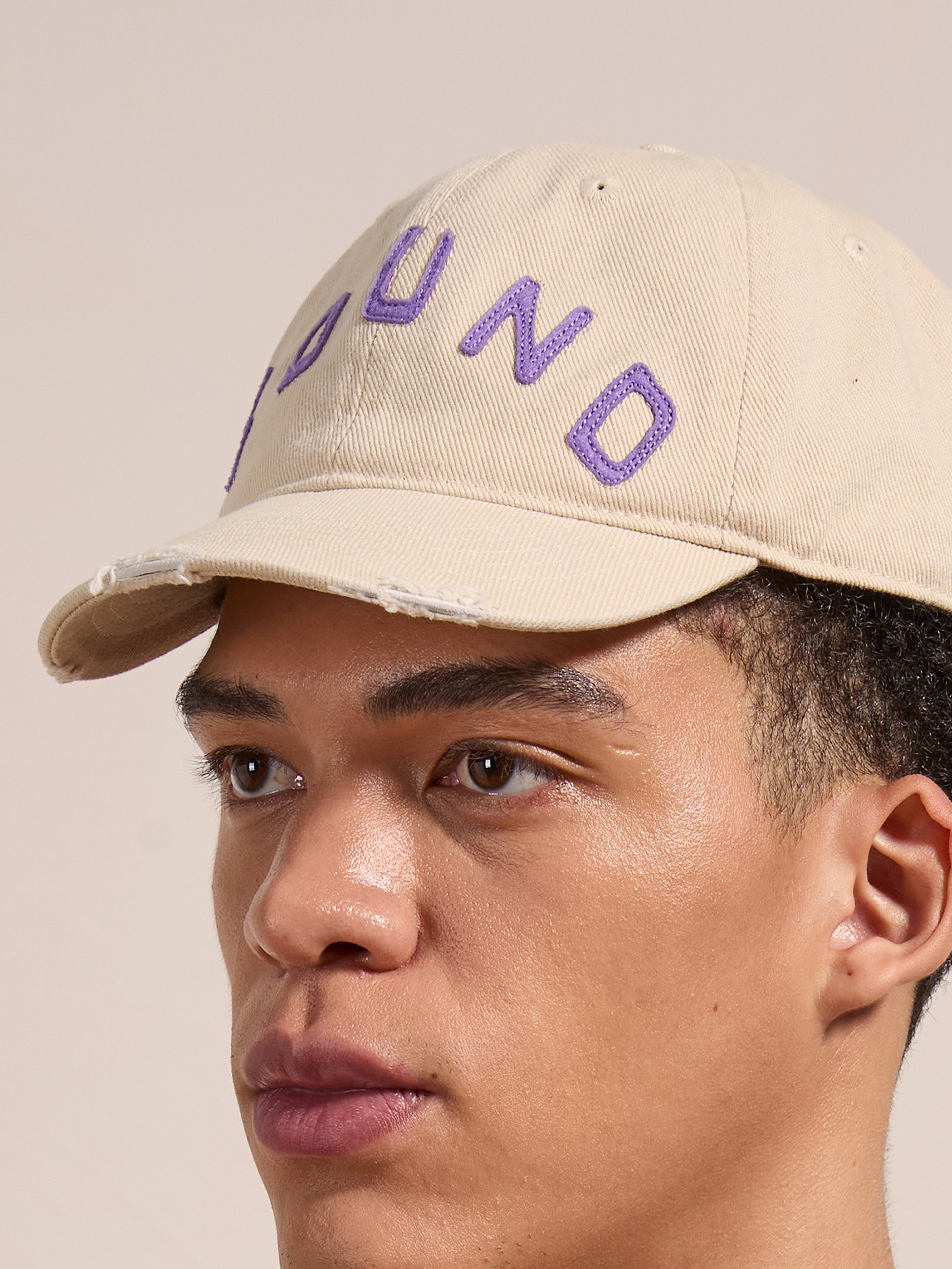 A person wearing the FOUND Ivory Felt Patch Cap, featuring a vintage wash, frayed edges, and purple embroidered letters partially spelling "FOUND.