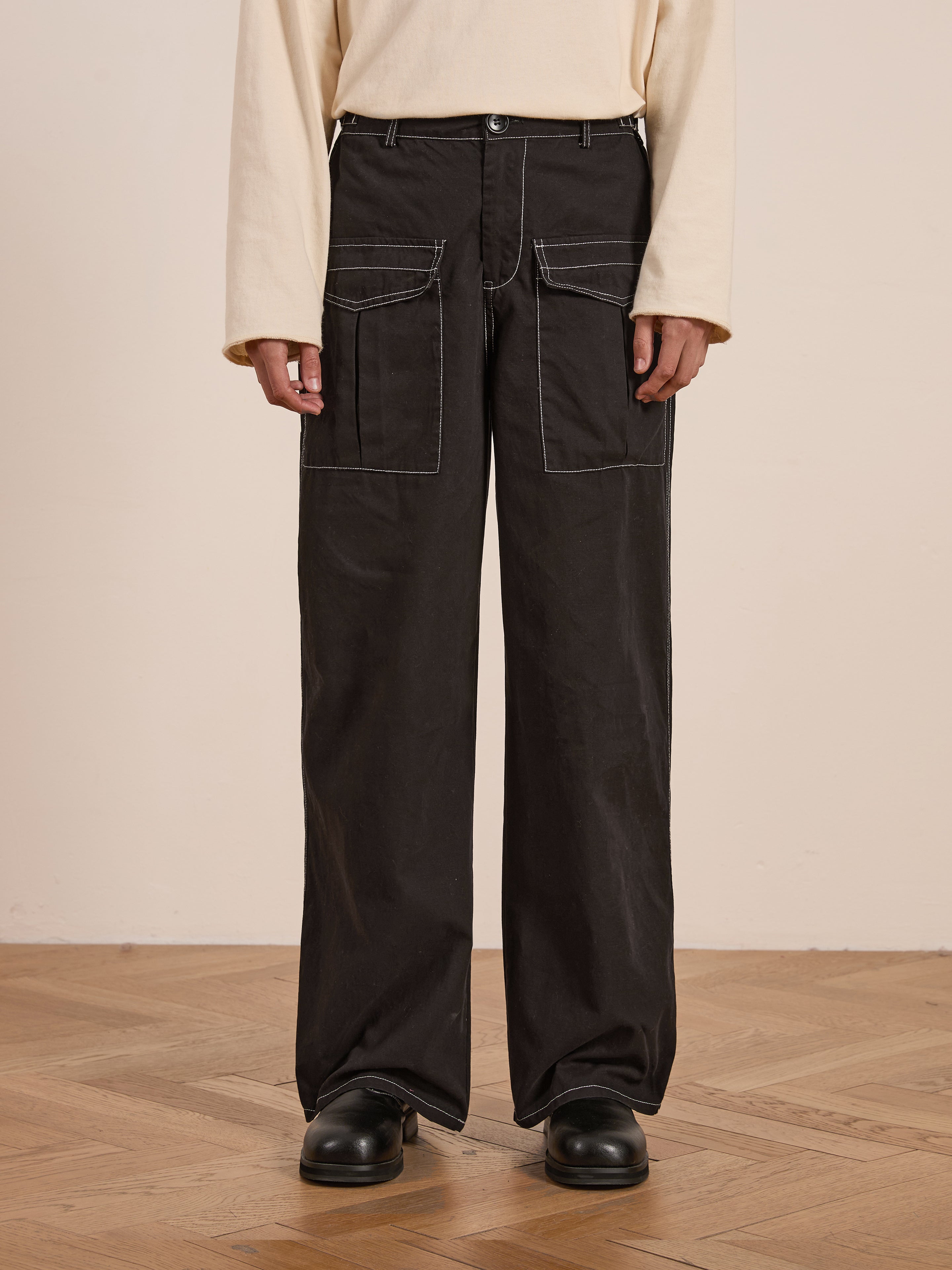 A person stands on a wooden floor wearing FOUND's Lucca Black Contrast Pocket Pants in midweight cotton twill with white stitching and black shoes, showcasing a relaxed straight-leg fit that enhances the casual yet stylish look.