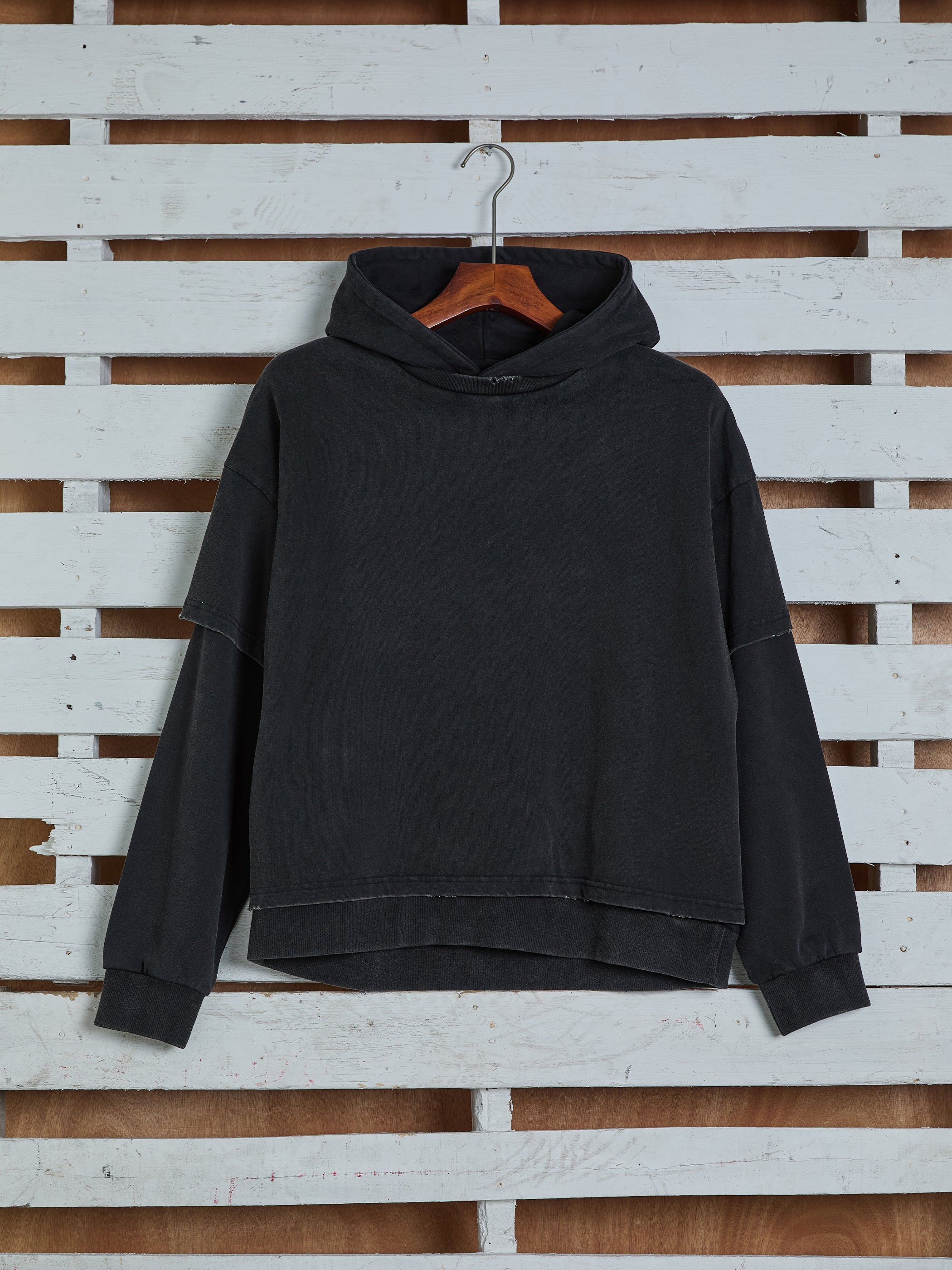 The "Double Layer Hoodie" by Found, crafted from soft French terry cotton, is displayed on a wooden hanger against a white wooden pallet backdrop.