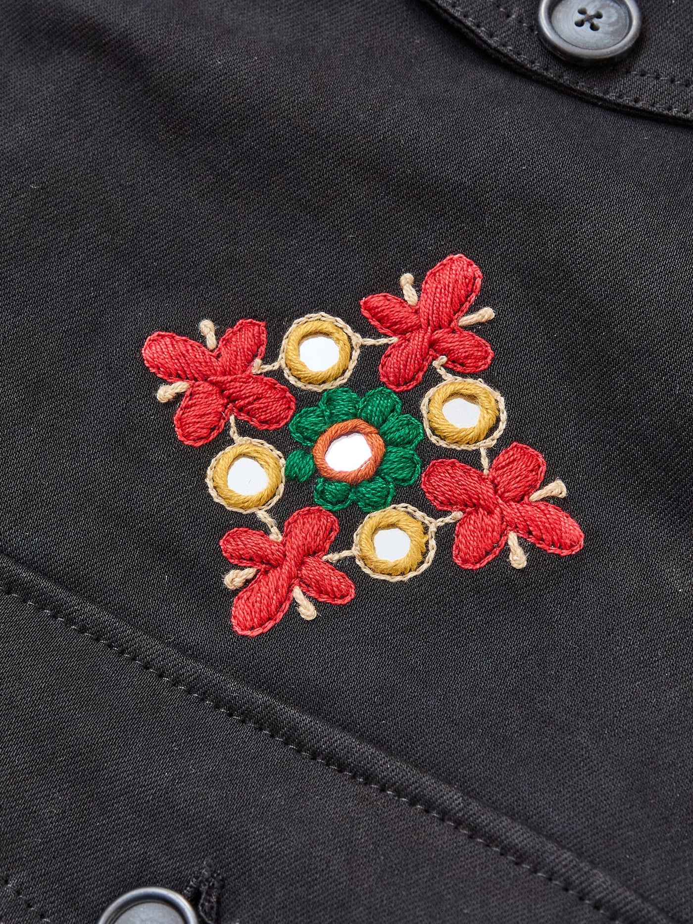 The Found Mirror Ornament Hand Embroidered Work Jacket features red and gold Aari and Sheeshakari embroidery with mirror accents, forming a striking floral design on black cotton twill near the buttons.