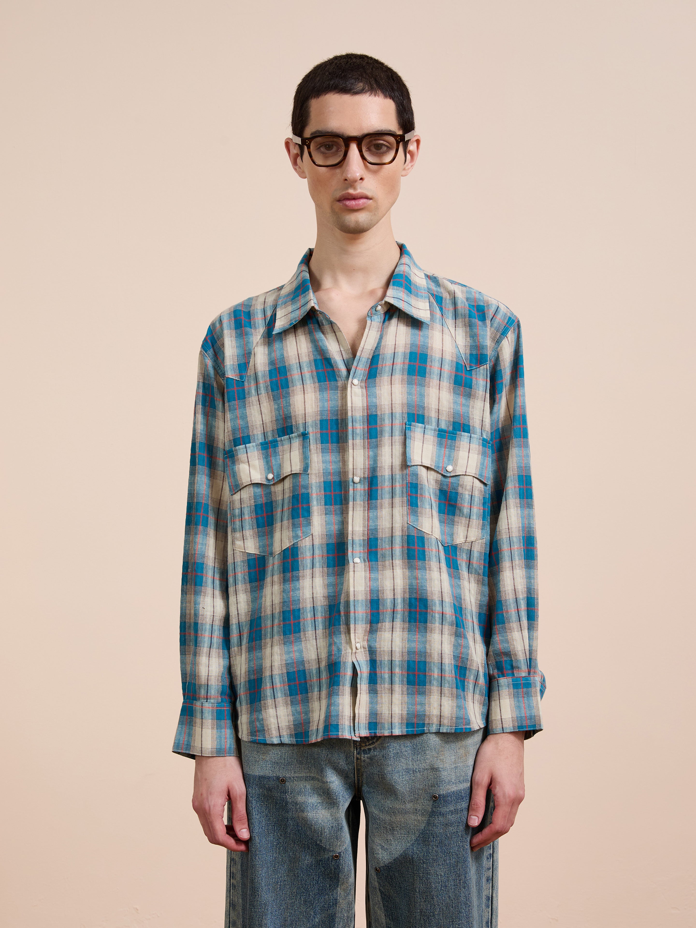 A person wearing glasses, blue jeans, and a FOUND Flannel Shirt in a unisex relaxed fit Western plaid stands facing forward against a plain beige background.